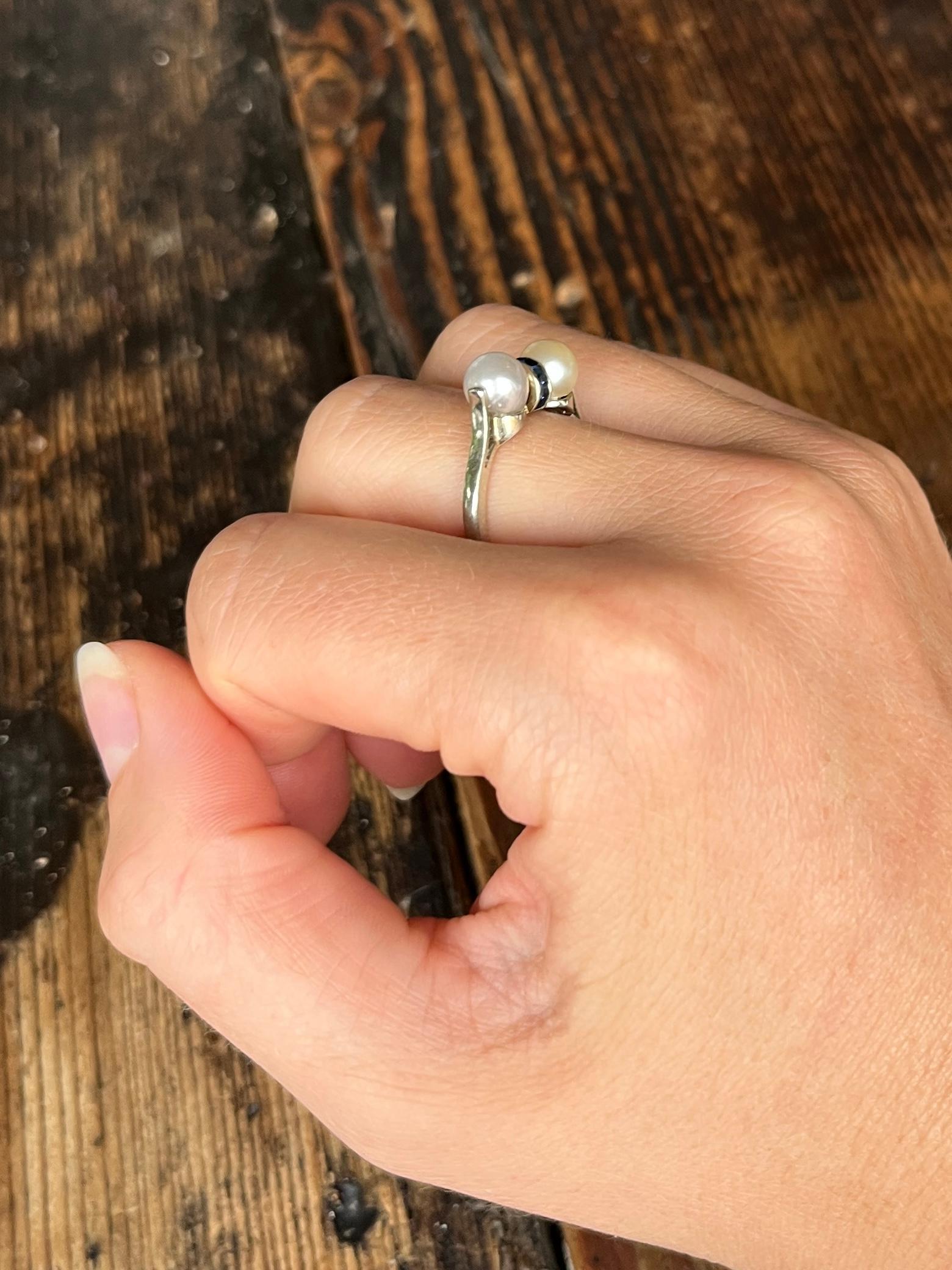 Dieser Ring enthält zwei Perlen, die sich im Farbton leicht unterscheiden, wie Sie auf den Bildern sehen können. Zwischen den Perlen befindet sich ein Band aus quadratisch geschliffenen Saphiren mit insgesamt 40 Pence. Der Ring ist aus 18 Karat