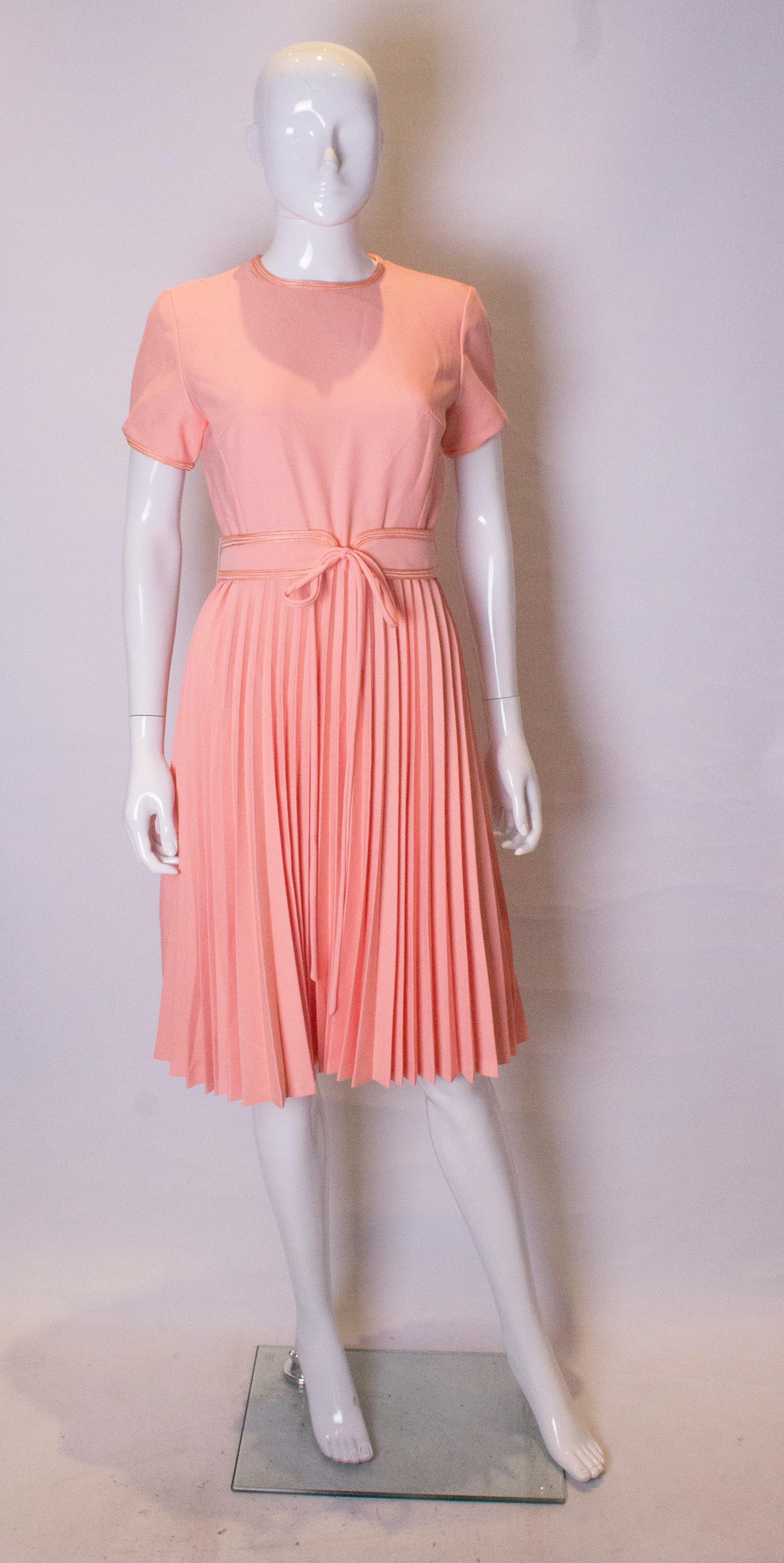 A pretty pink outfit by Peggy French Couture. The dress has a round neckline with short sleeves, a full pleated skirt and central back zip, and self fabric belt.  The jacket has a three button fastening and is edged in a matching pink braid.
Dress