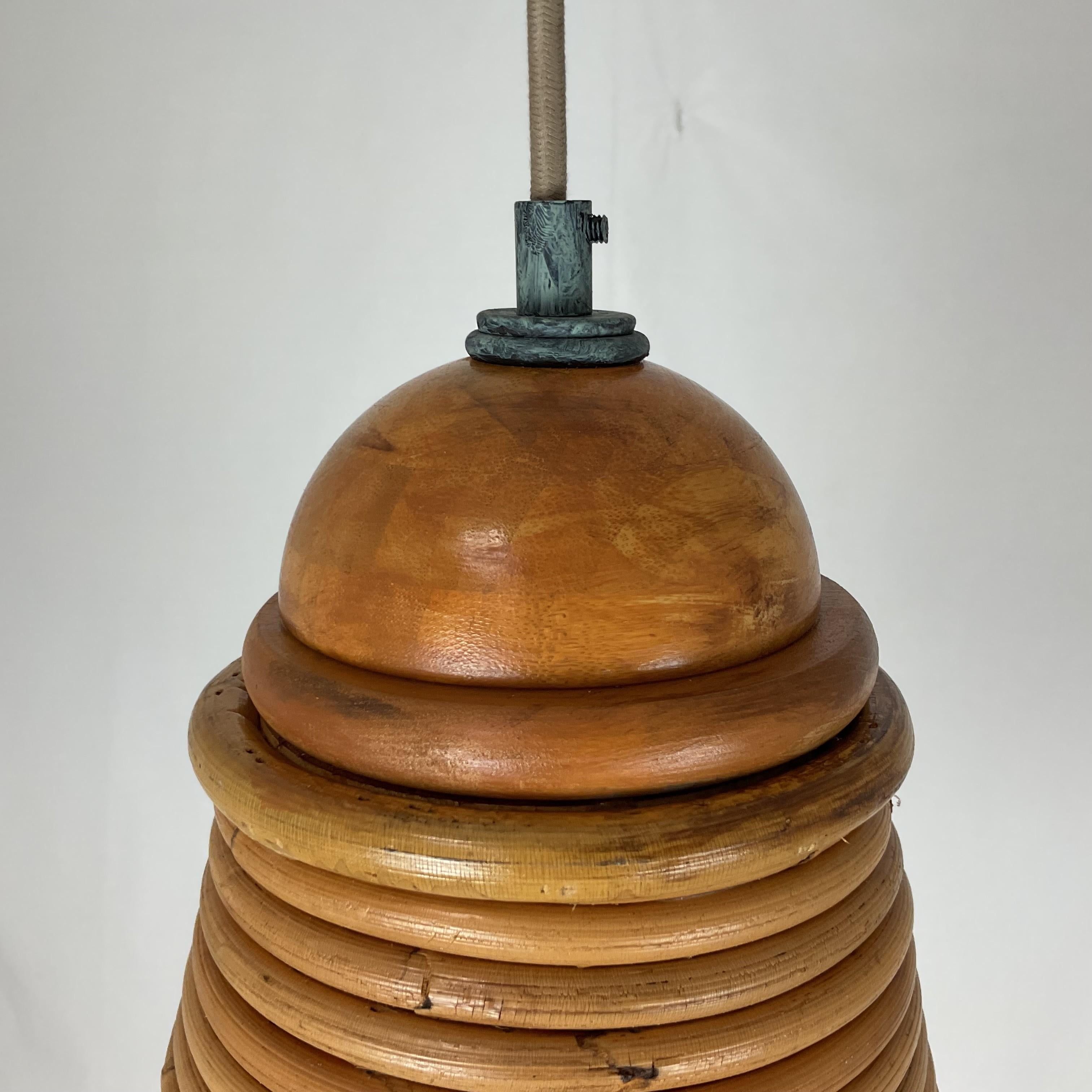 Questo lampadario a sospensione in rattan vintage dona calore, consistenza e carattere a qualsiasi ambiente. Realizzato a mano in una silhouette affusolata ispirata all'alveare, l'apparecchio è formato da spire di rattan naturale strettamente