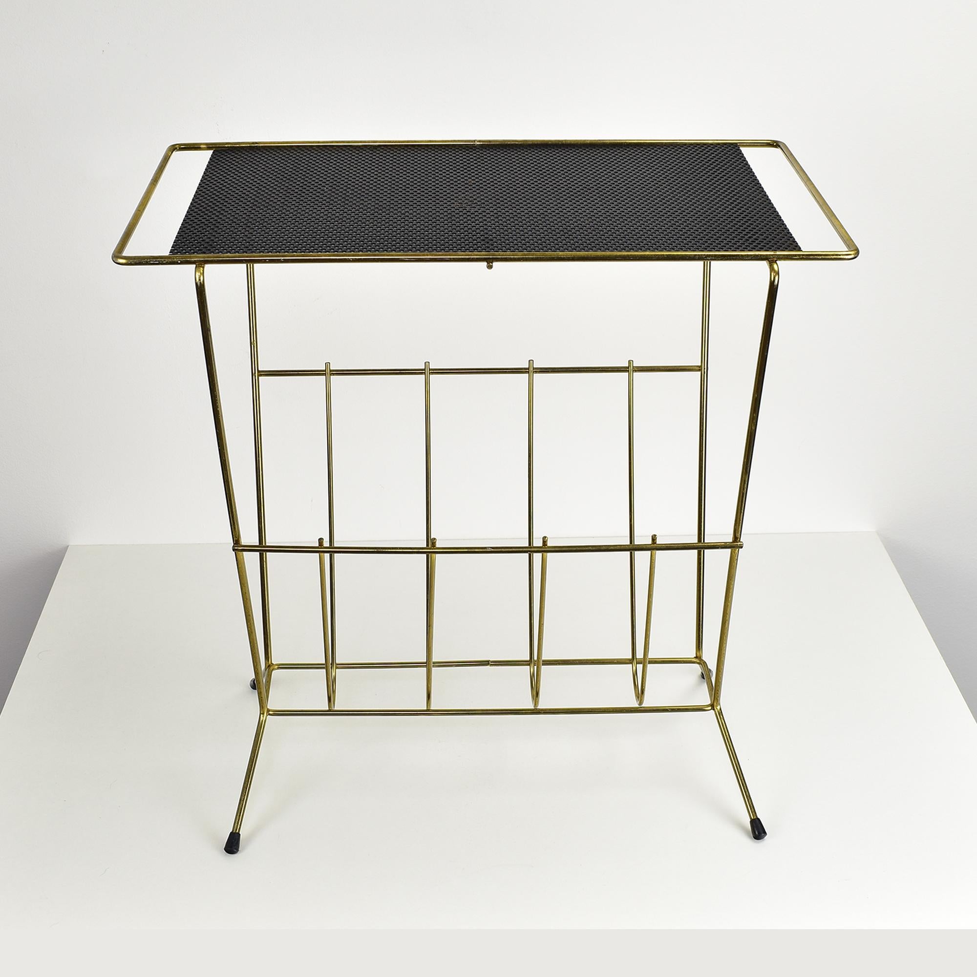 Il s'agit d'un porte-revues vintage qui sert également de table d'appoint ou de table de chevet. Le cadre est en laiton, ce qui lui confère une finition dorée et brillante, tandis que la surface supérieure est en métal perforé. La section