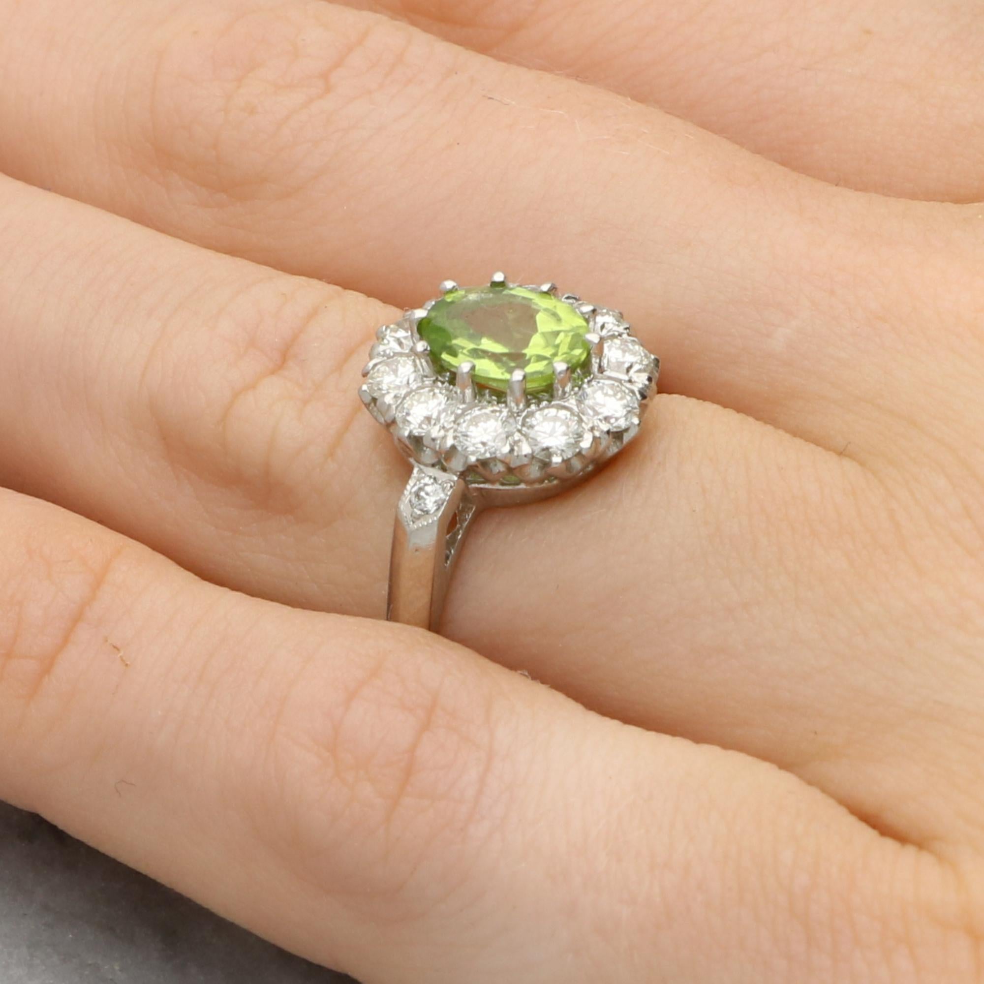 Ein klassischer Vintage-Ring mit Peridot und Diamanten, gefasst in Platin. 

Der Ring ist in der Mitte mit einem leuchtenden Peridot im Ovalschliff besetzt, der sicher in zehn Krallen gefasst ist. Der Peridot ist von einer Gruppe von zehn runden