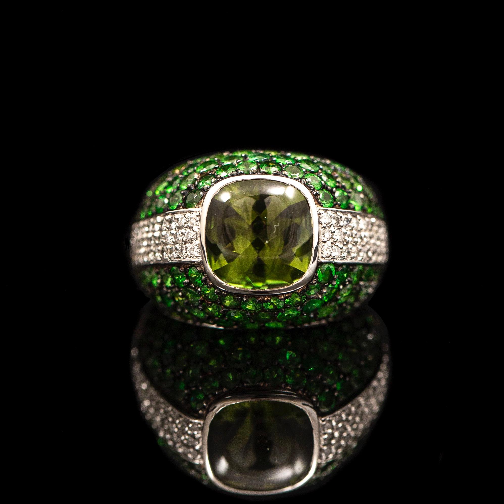 Vintage peridot, tsavorite garnet and diamond cocktail ring in 19.2kt white gold, Italy, late 20th century. This bombe ring features a cushion-shape buff-top yellowish-green peridot bezel-set to the center with a cabochon crown and a faceted