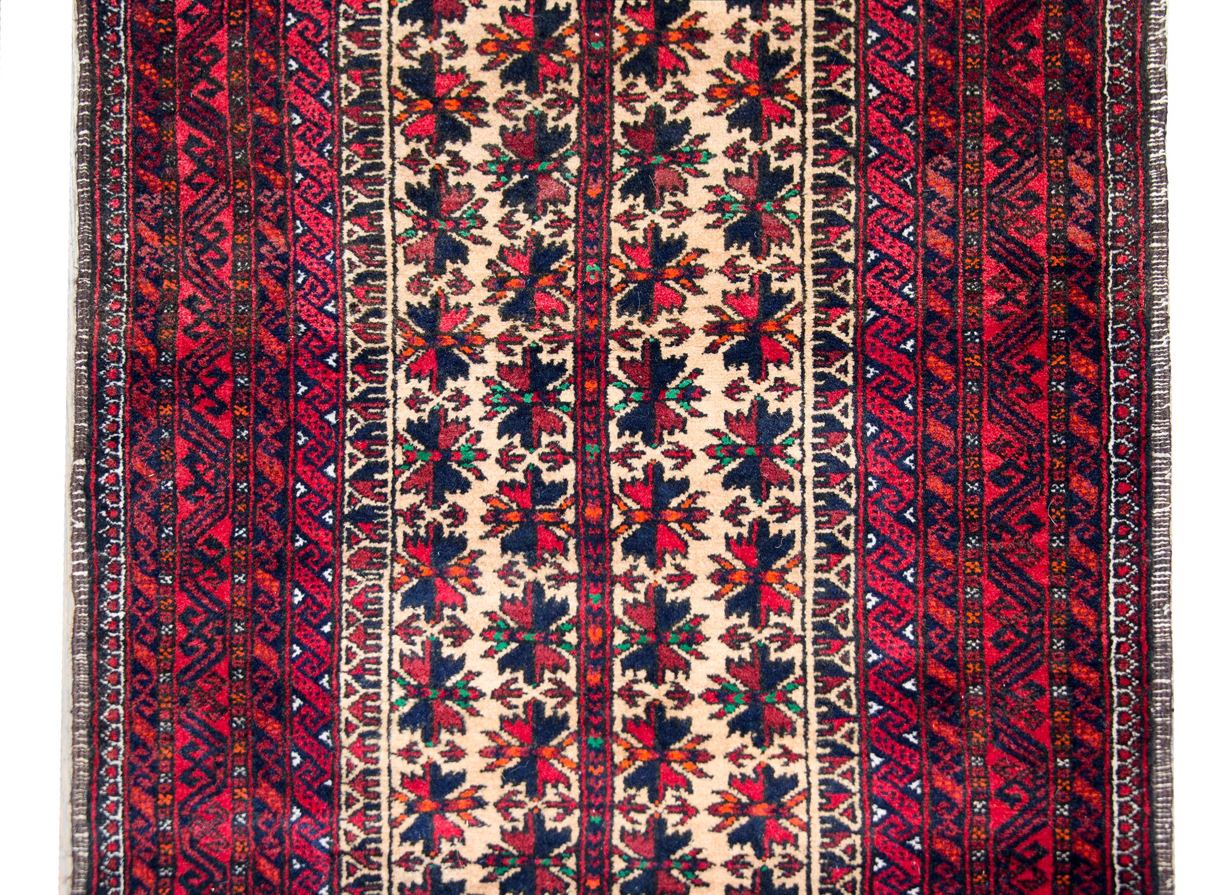 A beautiful mid-20th century Persian Baluch rug with a central stylized floral field surrounded by several petite geometric patterned stripes, and all woven in brilliant crimson, indigo, cream, green, and orange wool.