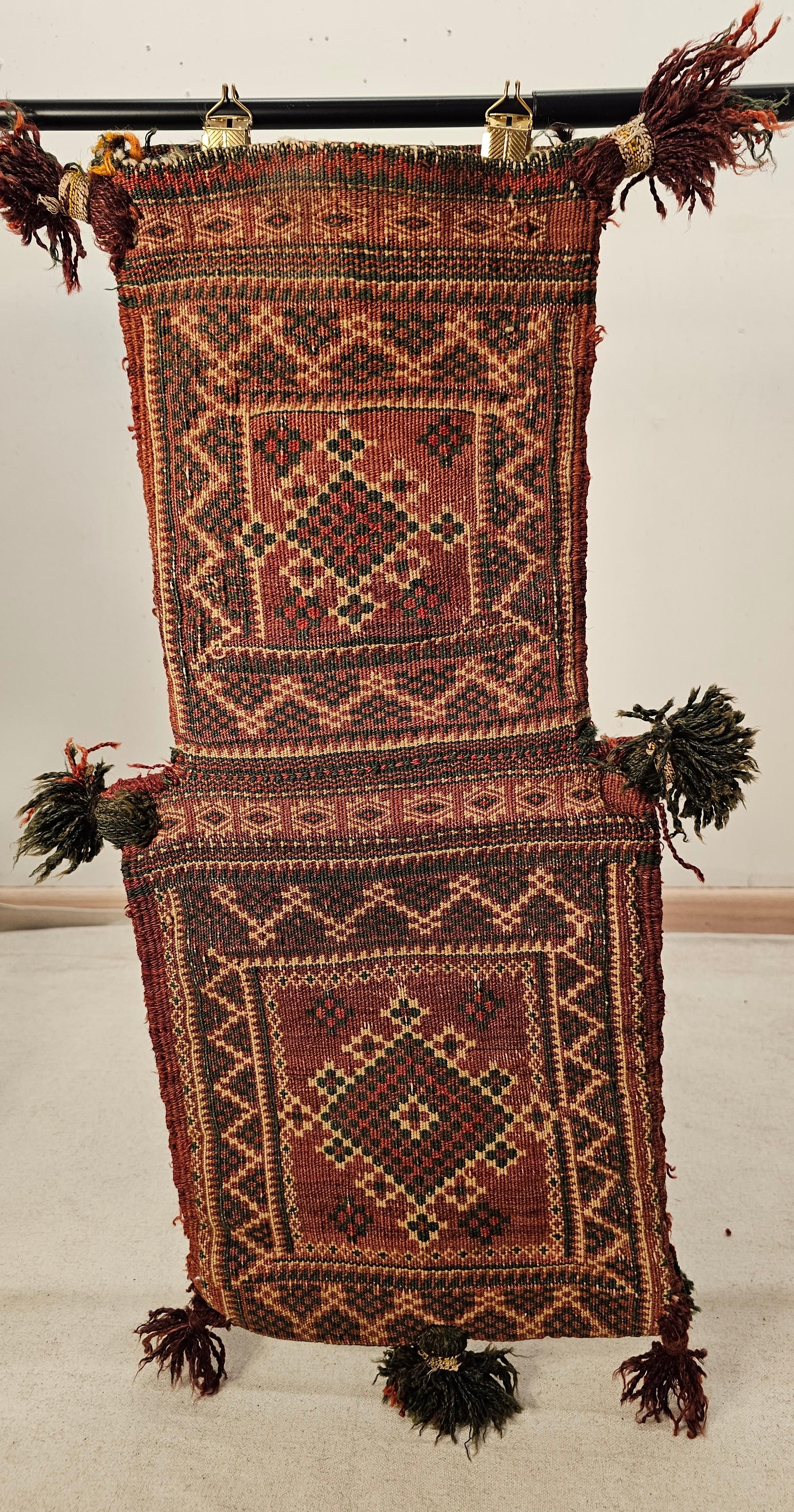 A vintage Baluch tribal salt bag with geometric pattern in green, red, ivory and brown colors from the early 1900s.  The salt bag has a small Baluch piled rug woven for the front and the back of the bag which is very unusual since most salt bags