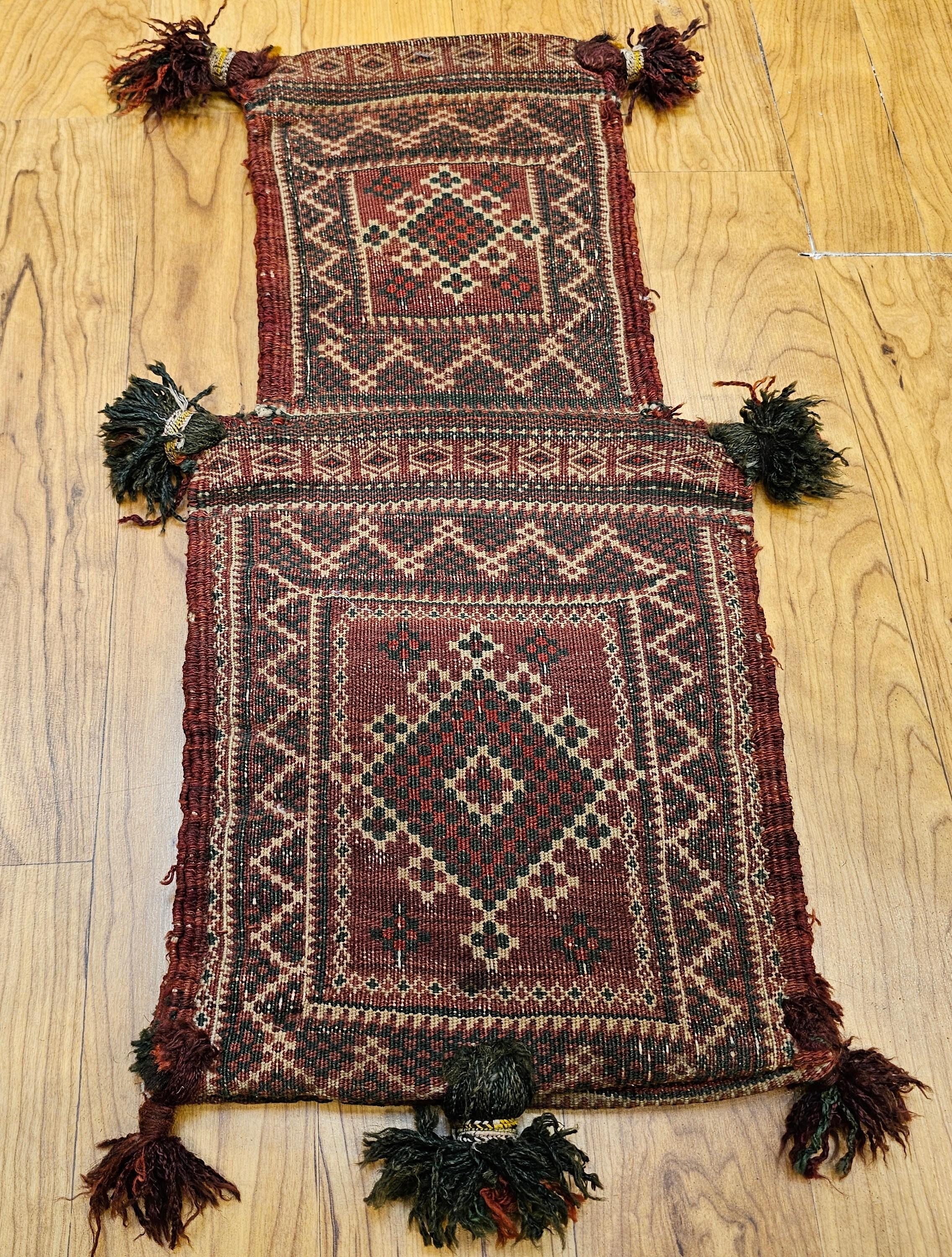Bolsa de sal tribal baluch vintage con motivos geométricos en colores verde, rojo, marfil y marrón de principios del siglo XX.  La bolsa de sal tiene una pequeña alfombra baluch tejida en la parte delantera y trasera, lo cual es muy poco habitual,