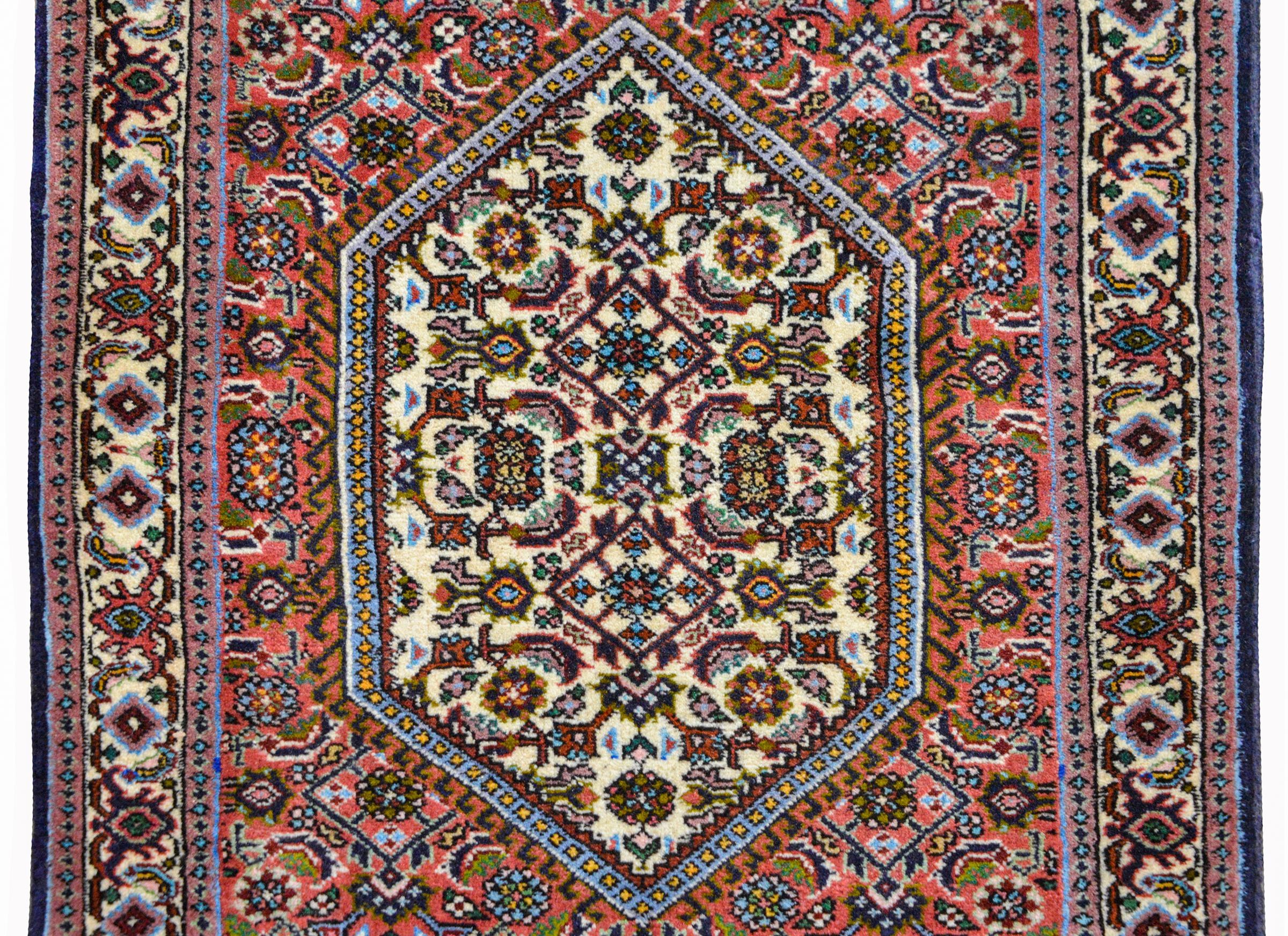 A wonderful vintage Persian Bidjar rug with a diamond medallion with a stylized floral pattern amidst a field of more stylized flowers and surrounded by a stylized floral and scrolling vine border, all woven in coral, green, indigo, and violet,