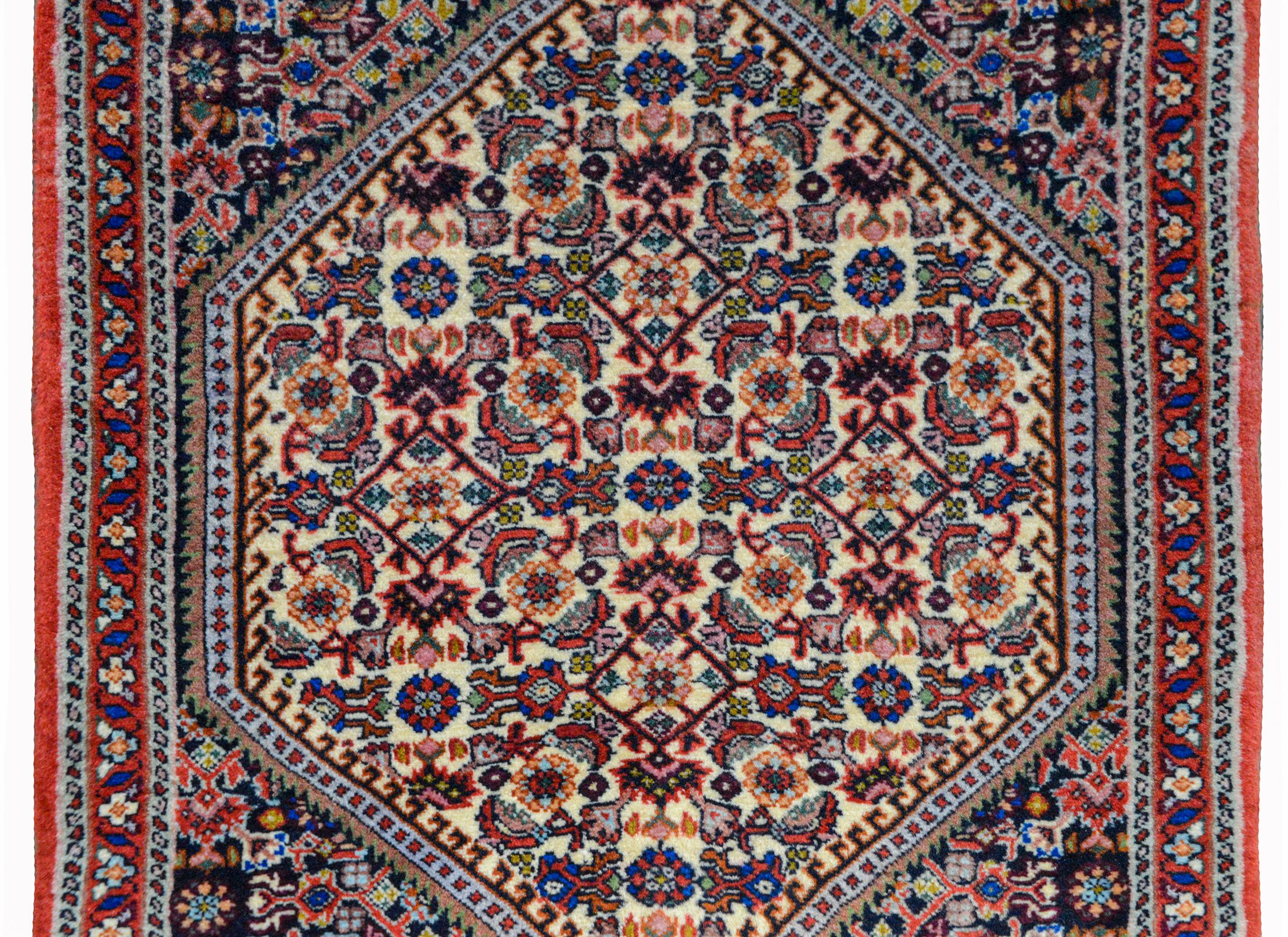 A wonderful vintage Persian Bidjar rug with a diamond medallion with a stylized floral pattern amidst a field of more stylized flowers and surrounded by a stylized floral and scrolling vine border, all woven in red, pink, lavender, and indigo