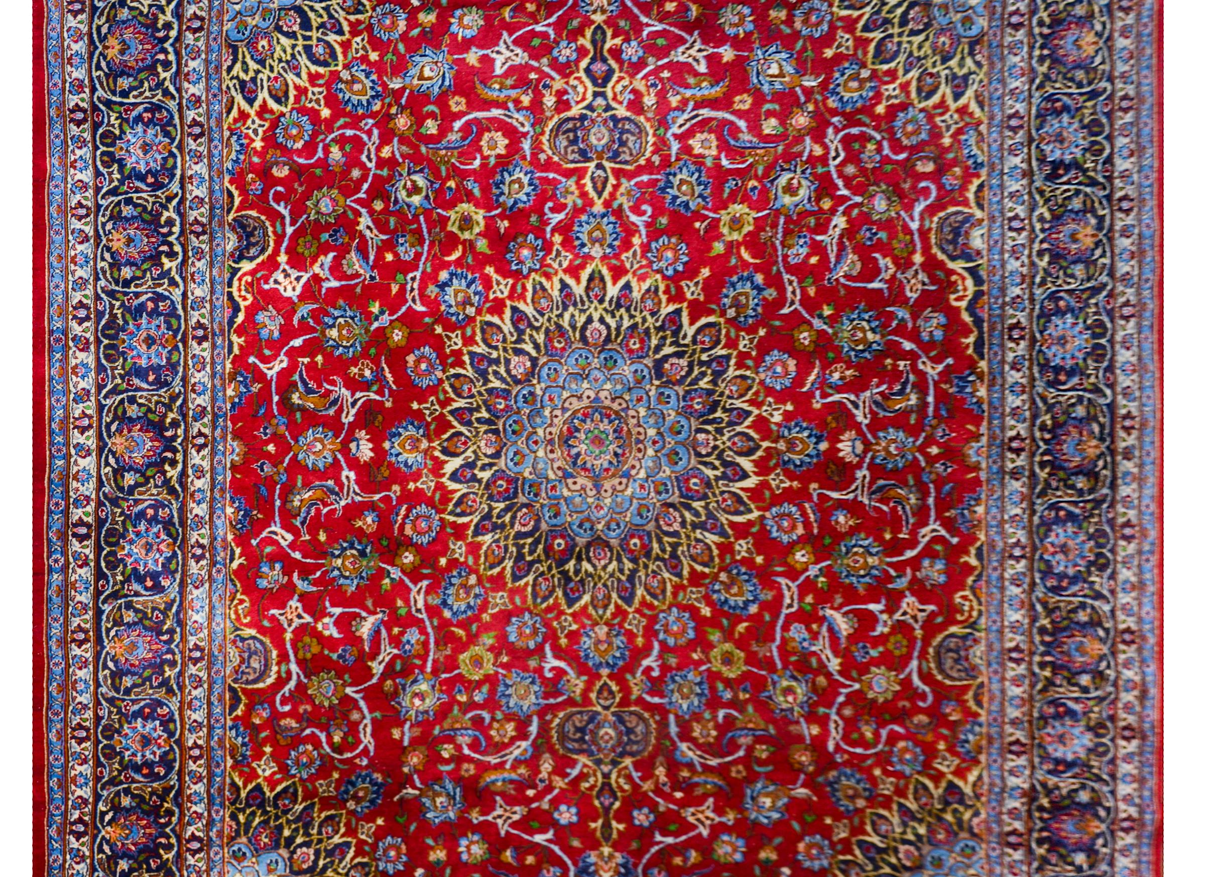 A beautiful vintage Persian Birjand rug with a large central medallion woven in rich indigos, golds, and greens, amidst a field of flowers and scrolling vines against a crimson background. The border is wide with multiple floral and scrolling
