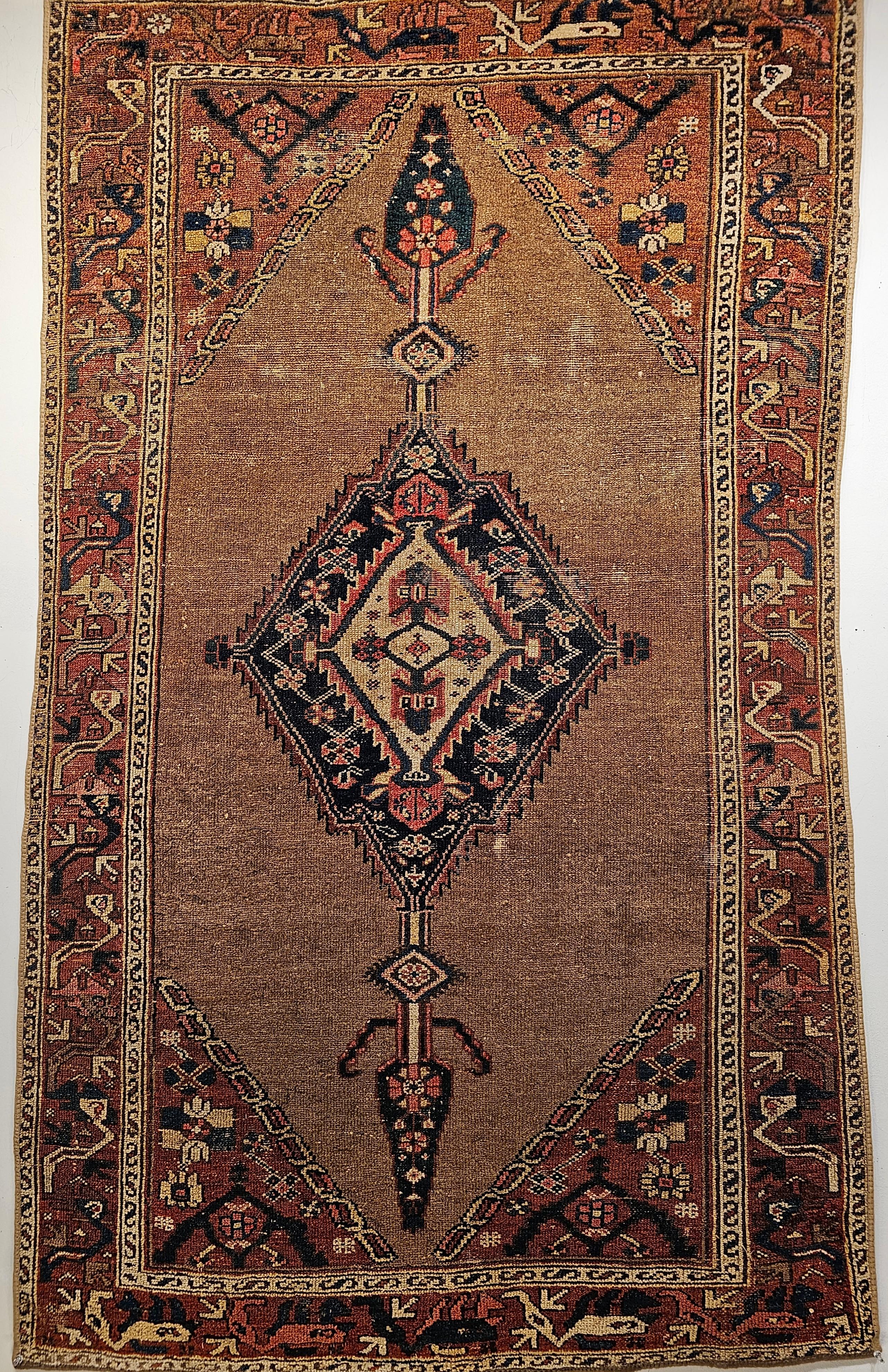 Vintage Persian Camelhair Malayer Area Rug with a central medallion in a geometric pattern is from the early 1900s.   The rug has an open field design with the elongated medallion in navy blue and ivory colors set on a camelhair background.  The