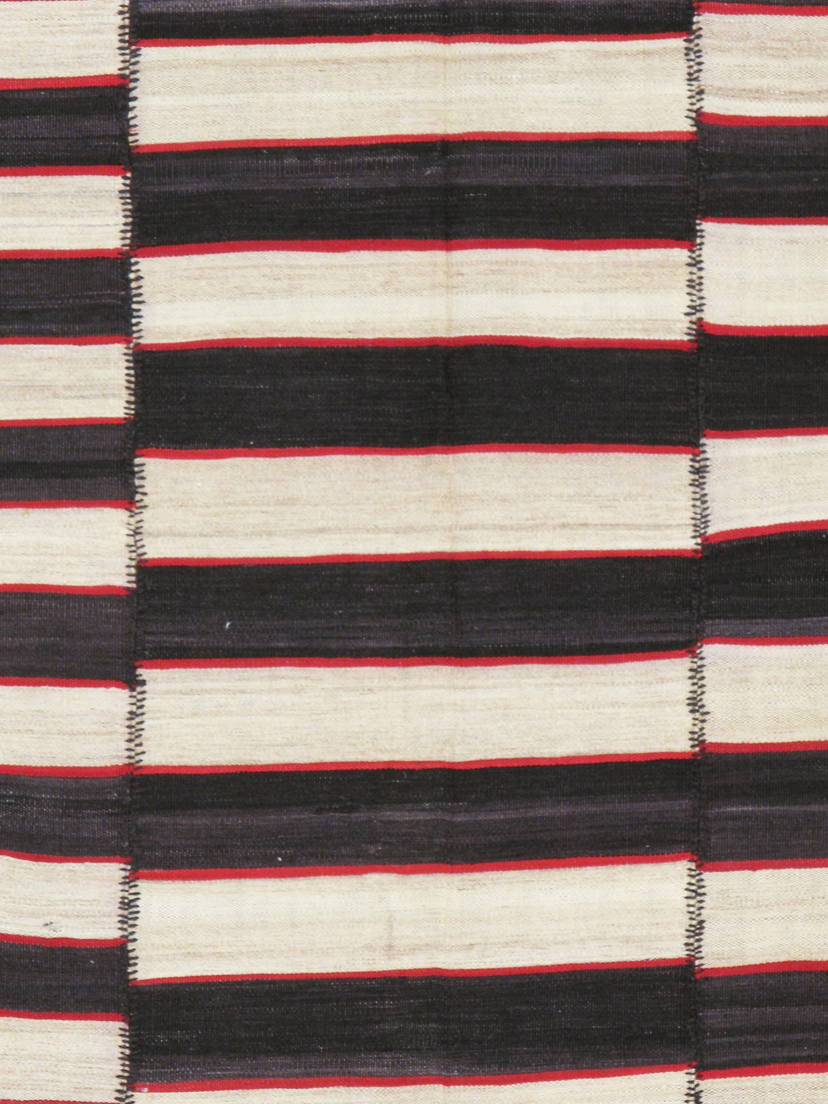 A vintage Persian flat-weave Kilim from the mid-20th century. Totally graphic and chic, this five-panel composite pileless carpet has black and ecru stripes alternating and slightly staggered overall with red narrow stripes joining the two. No