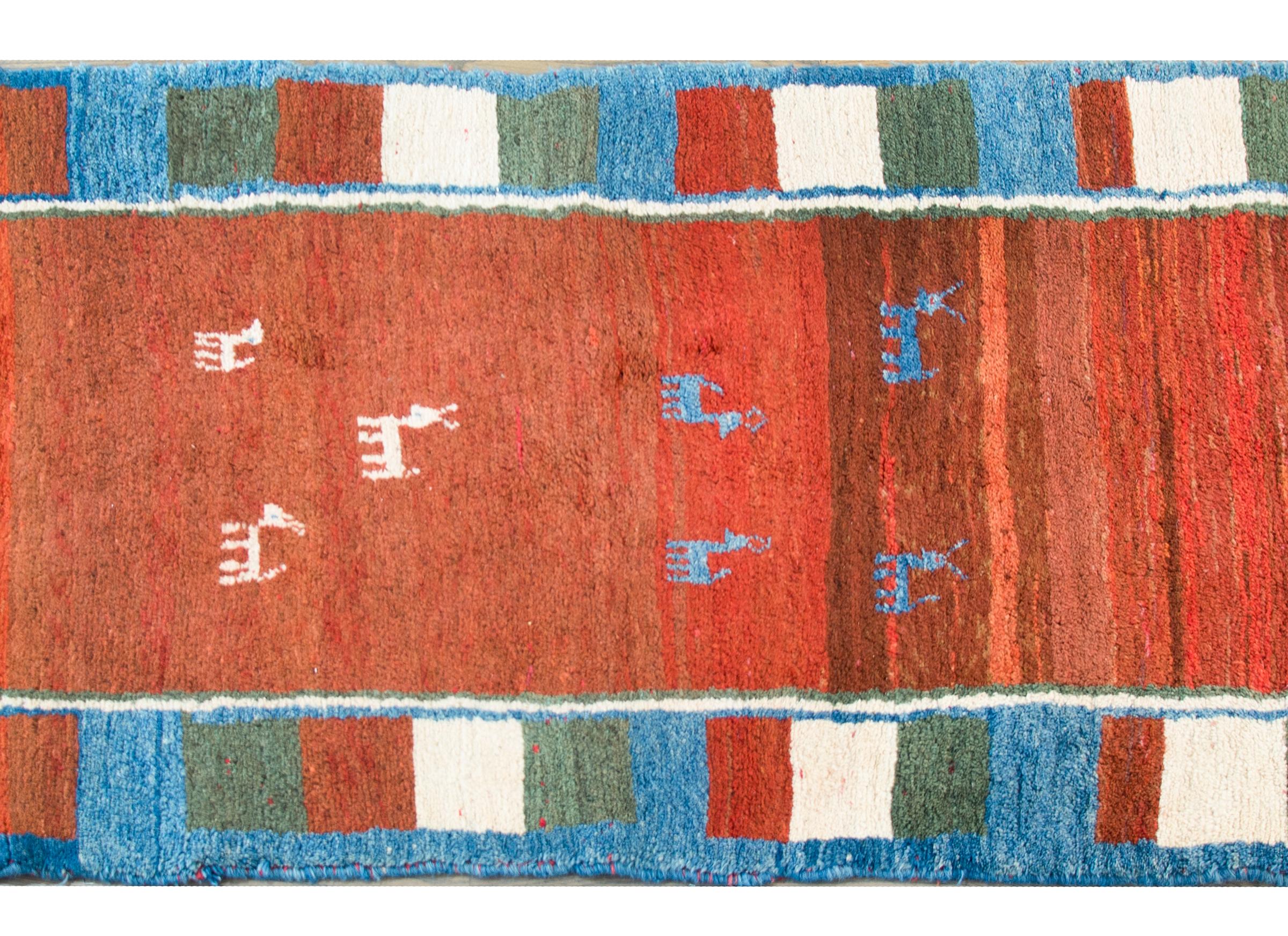 A beautiful bold vintage Persian Gabbeh rug with a n abrash crimson field with several indigo and white goats, and surrounded by a repeated crimson, white, green, and indigo square patterned border.