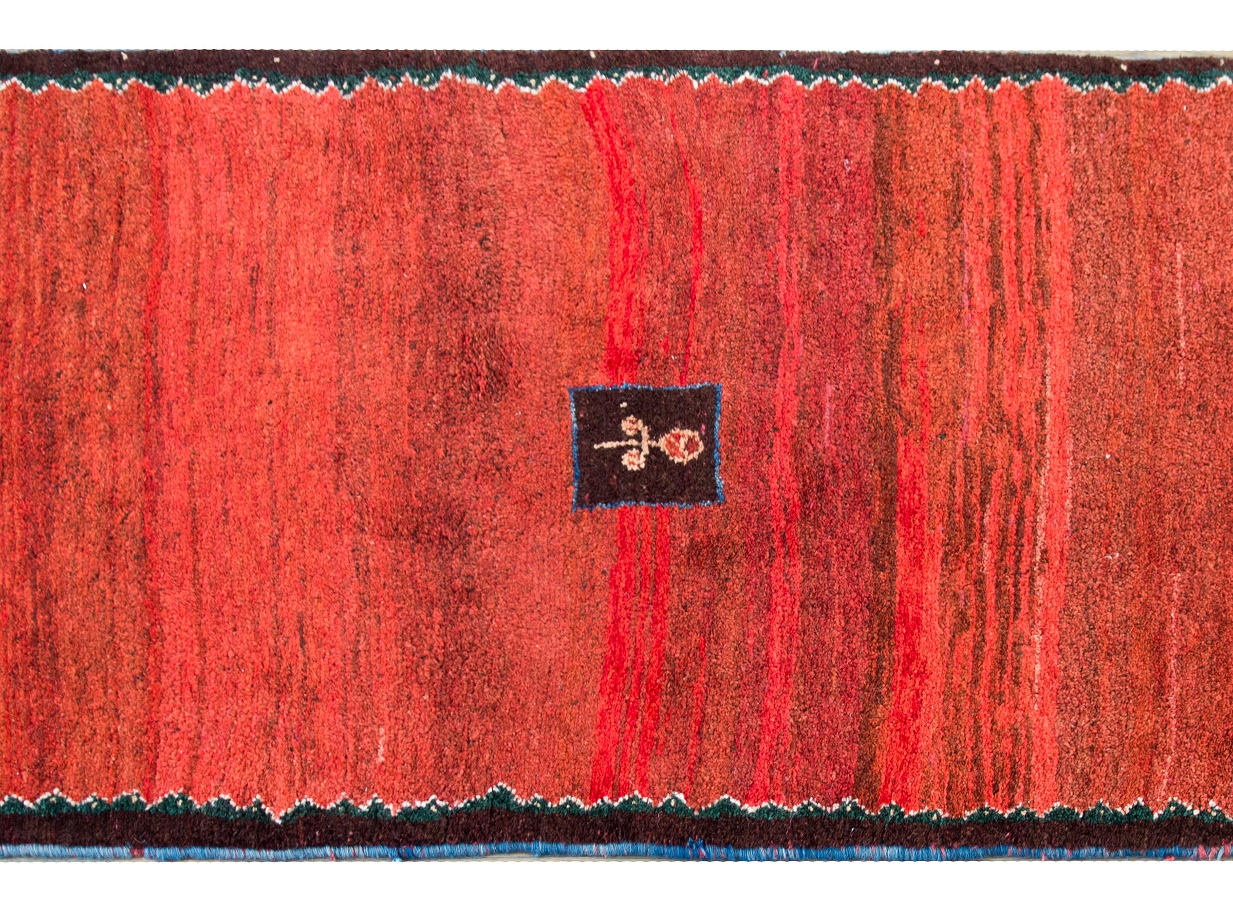 A wonderful mid-20th century Persian Gabbeh rug with a fantastic abrash crimson field with a small central floral medallion and another flower in each corner. The border is simple with a thin zigzag pattern woven in indigo, gold, and black.