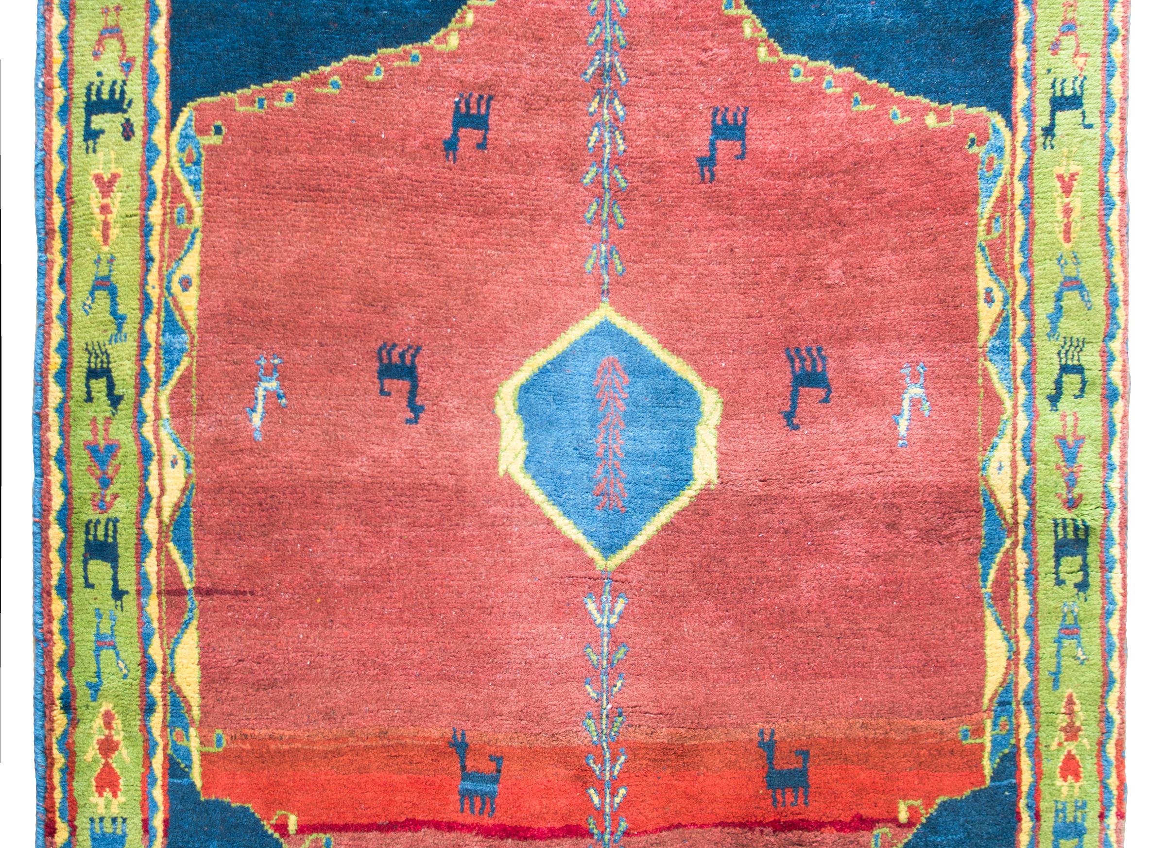 A fantastic mid-20th century Persian Gabbeh rug with an abrash crimson field dotted with indigo goats and chickens, and surrounded by a wide border with a whimsical pattern of repeated goats, chickens, people and stylized flowers, woven in light and
