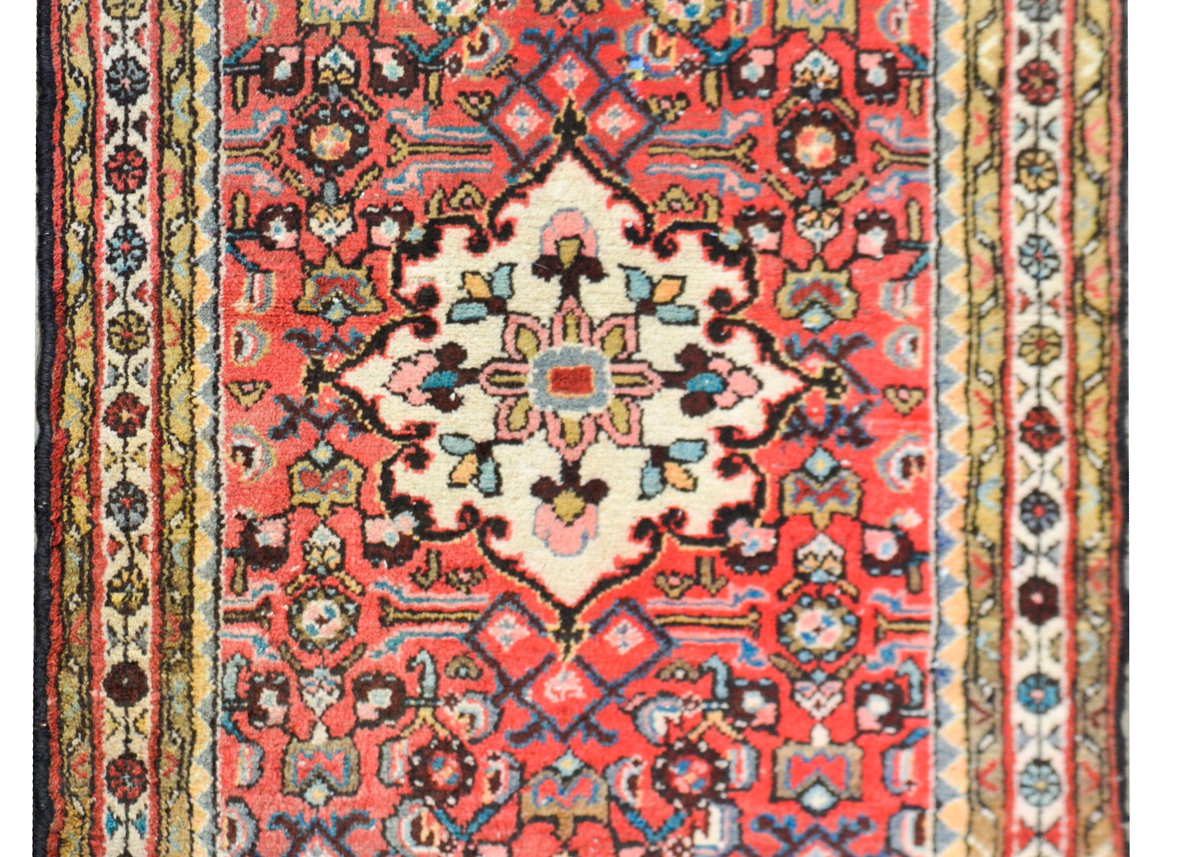 A sweet 20th century Persian Hamadan rug with a floral patterned medallion set against a background with scrolling vines and more stylized flowers, and surrounded by multiple petite floral patterned stripes.