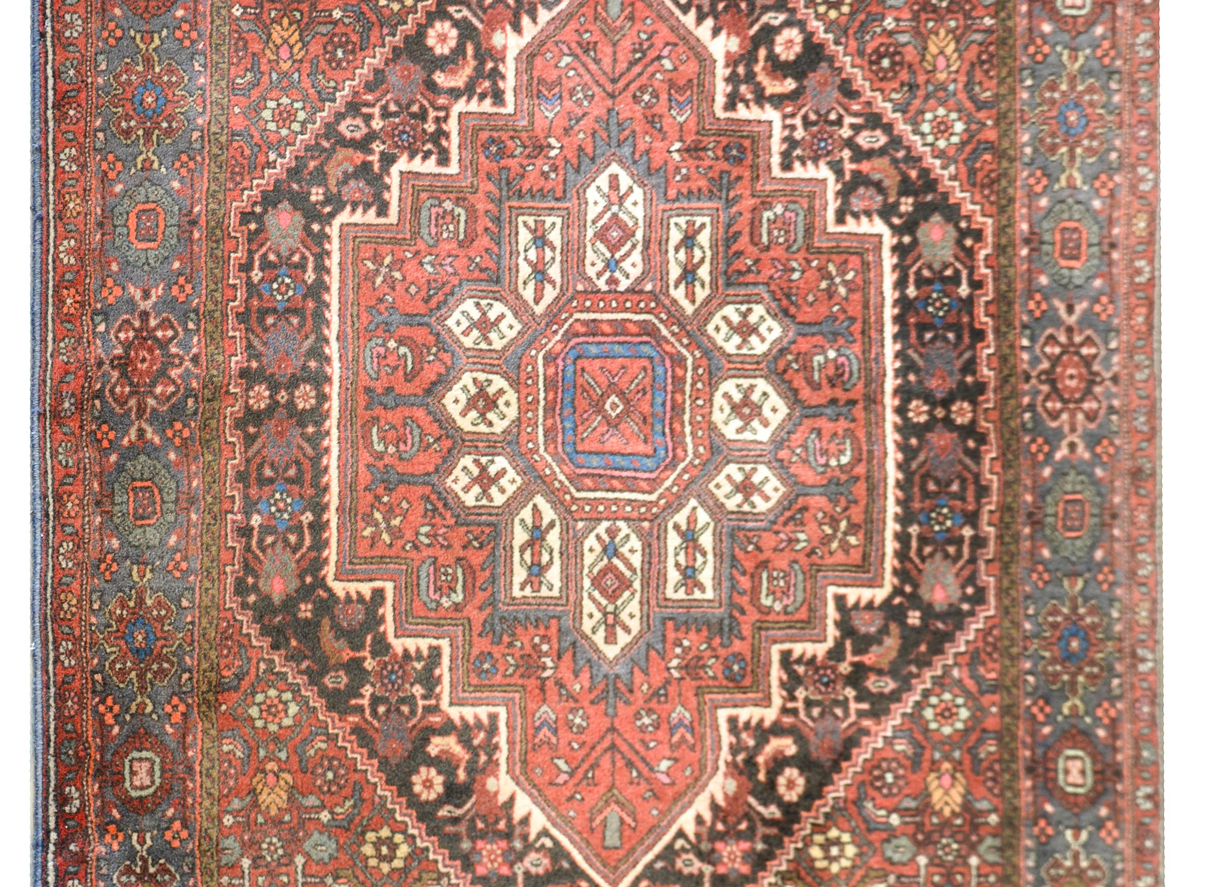 Un beau tapis vintage persan Hamadan avec un médaillon floral en forme de diamant au milieu d'un champ de fleurs et de vignes défilantes, et entouré d'une large bordure à motifs floraux.
