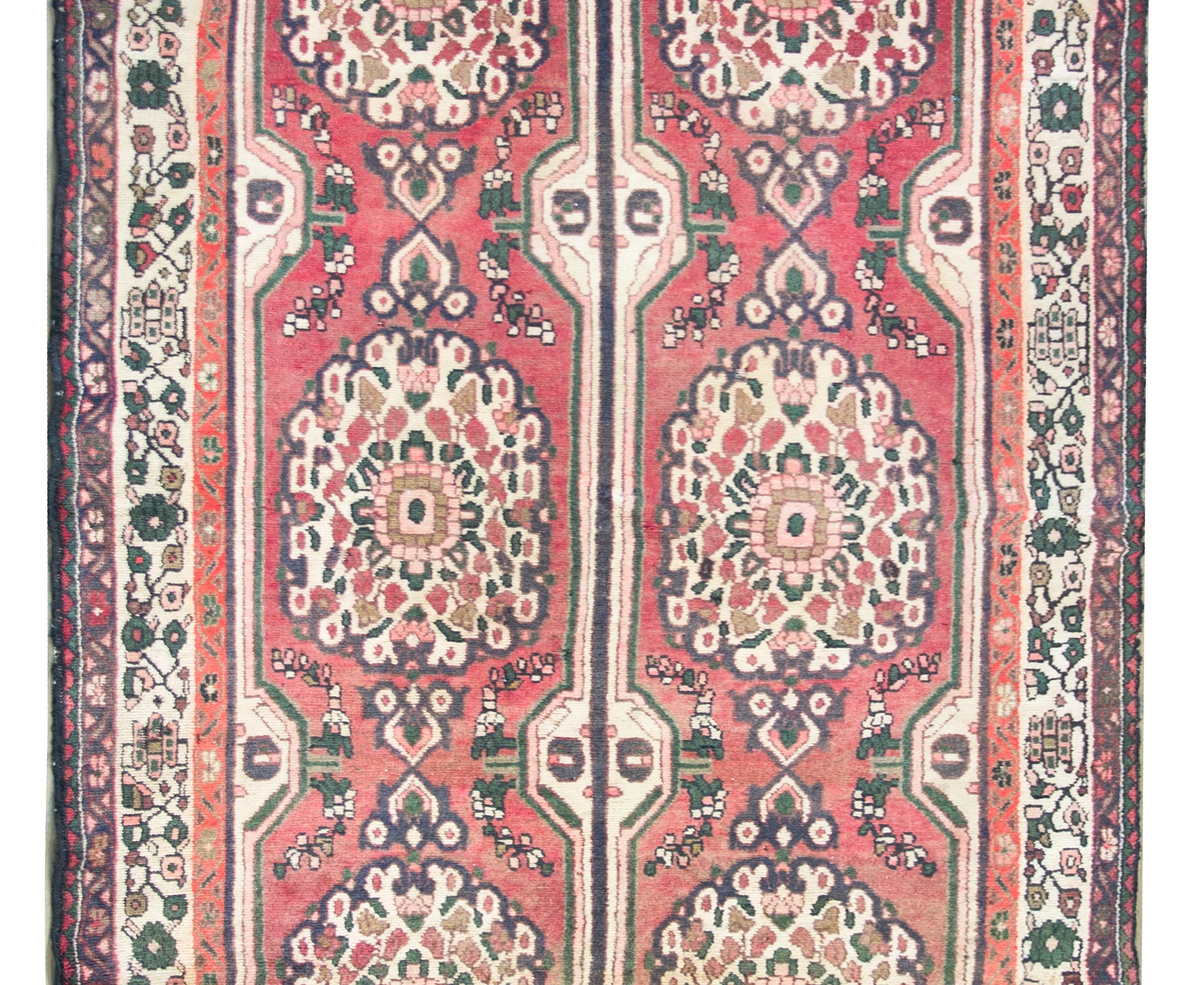 A wonderful mid-20th century Persian Hamadan rug with six large floral medallions living amidst a field of more flowers, and all woven crimson, beige, white, and pink wool. The border is complex with three distinct floral patterned stripes woven in