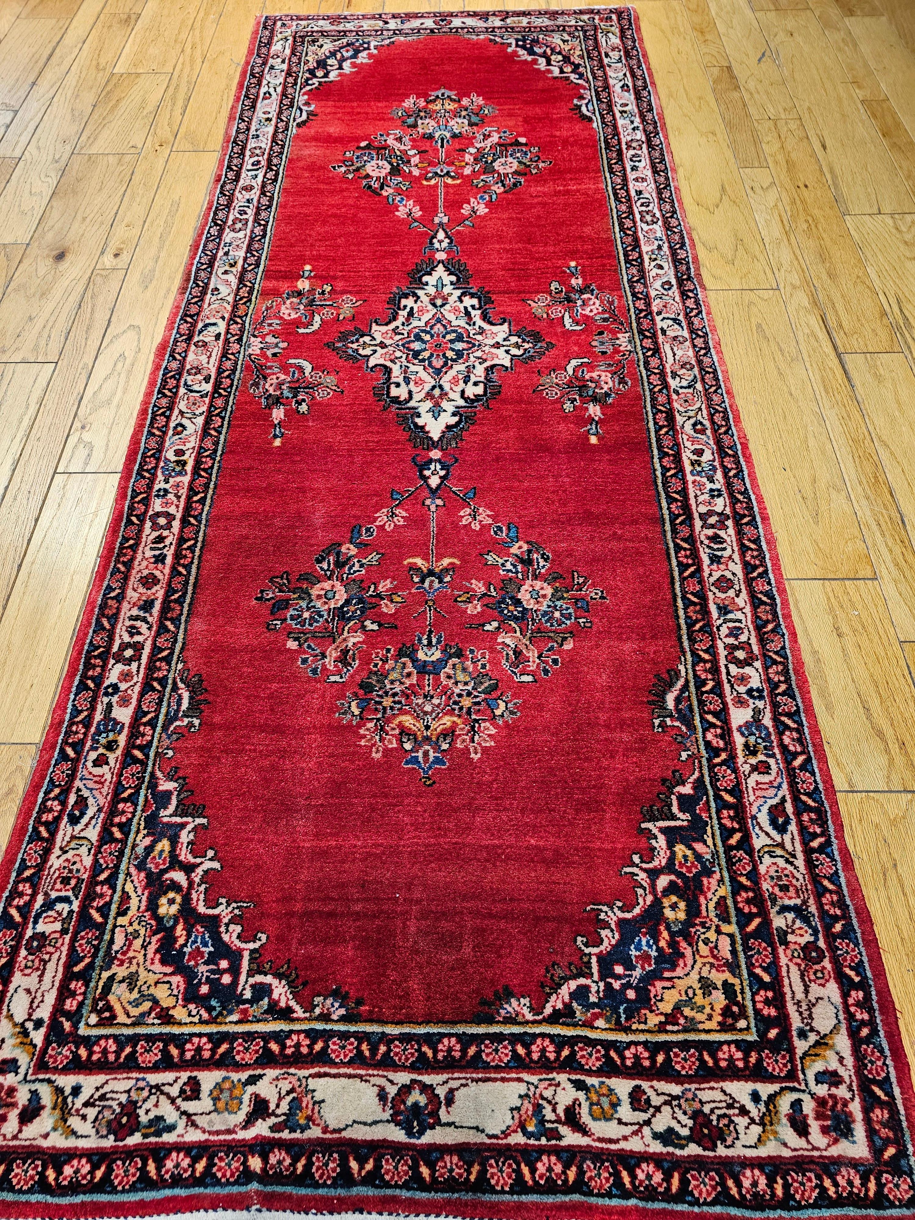  Hamadan wide runner from Western Persia is in a brilliant red color field.  It has a small central medallion in a cream color.  The border is also in a cream color and designs in red, green, blue, and yellow throughout the border.  The runner has a