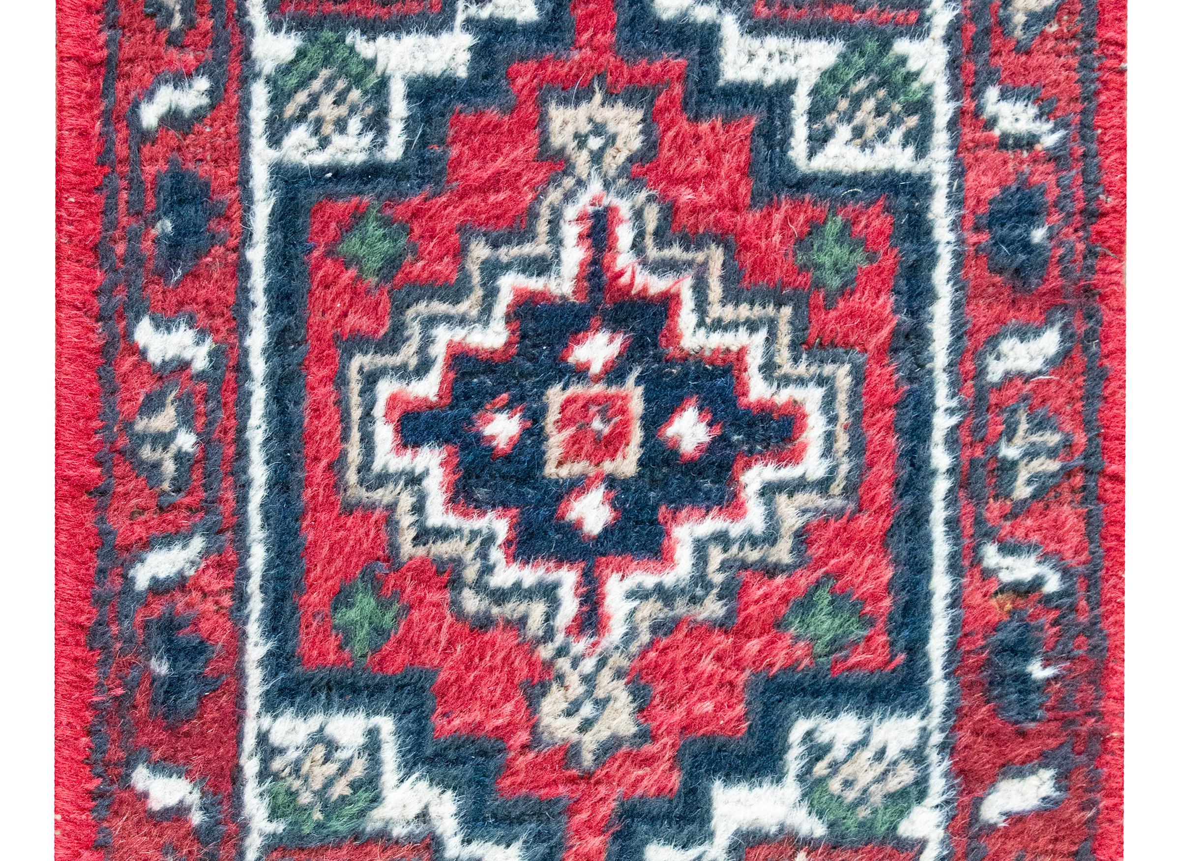 Un piccolo e affascinante tappeto persiano Hamadan della fine del XX secolo con un medaglione centrale a motivi geometrici circondato da un semplice bordo con motivi di foglie e viti a scorrimento, il tutto tessuto in lana color cremisi, indaco,