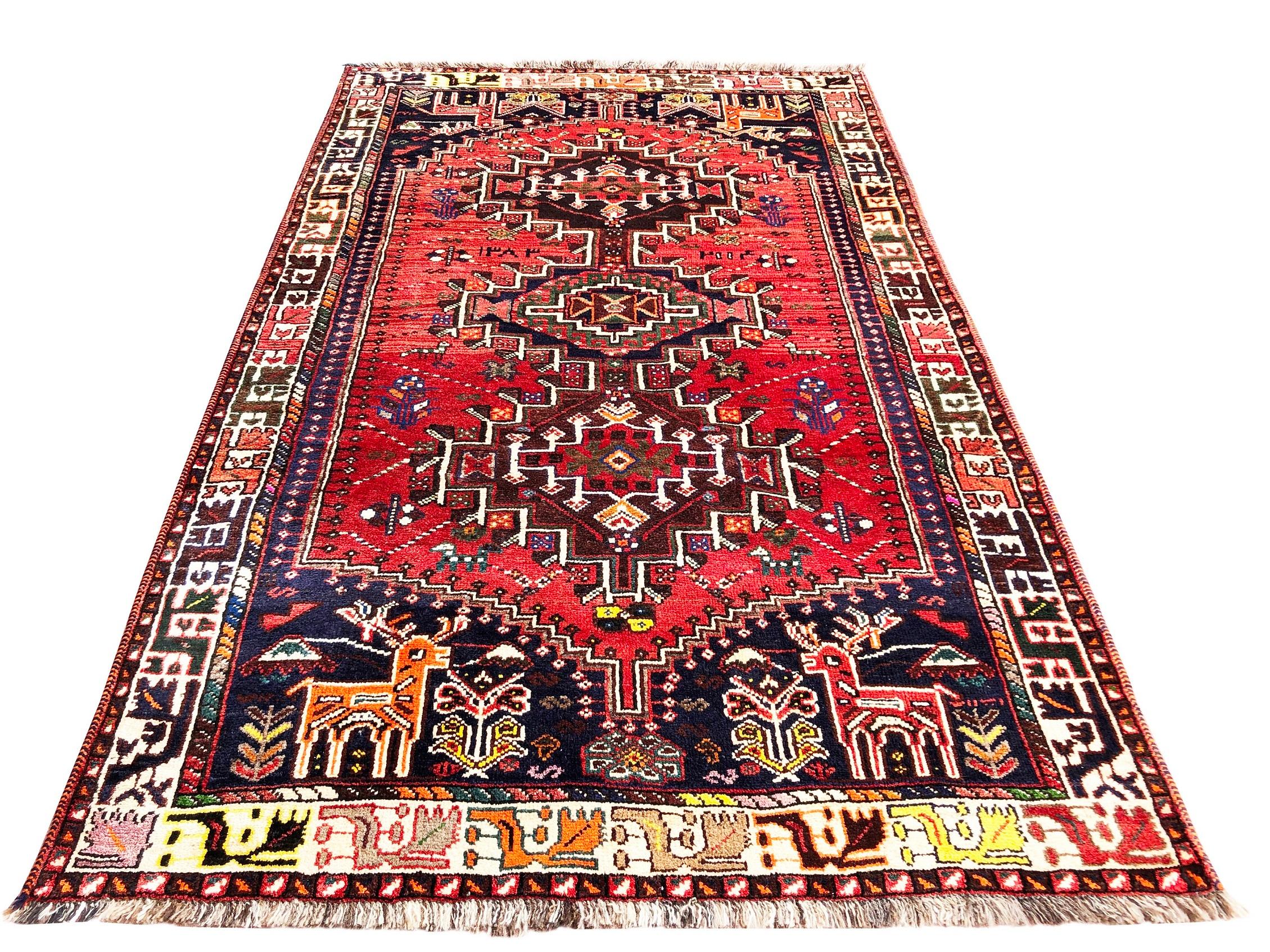 This rug is an authentic rug from Iran, Shiraz. The pile and foundation are wool. The base color is a vibrant red field with accents of bright orange, yellow, blue and green throughout with cream and multi border color. The design is geometric with