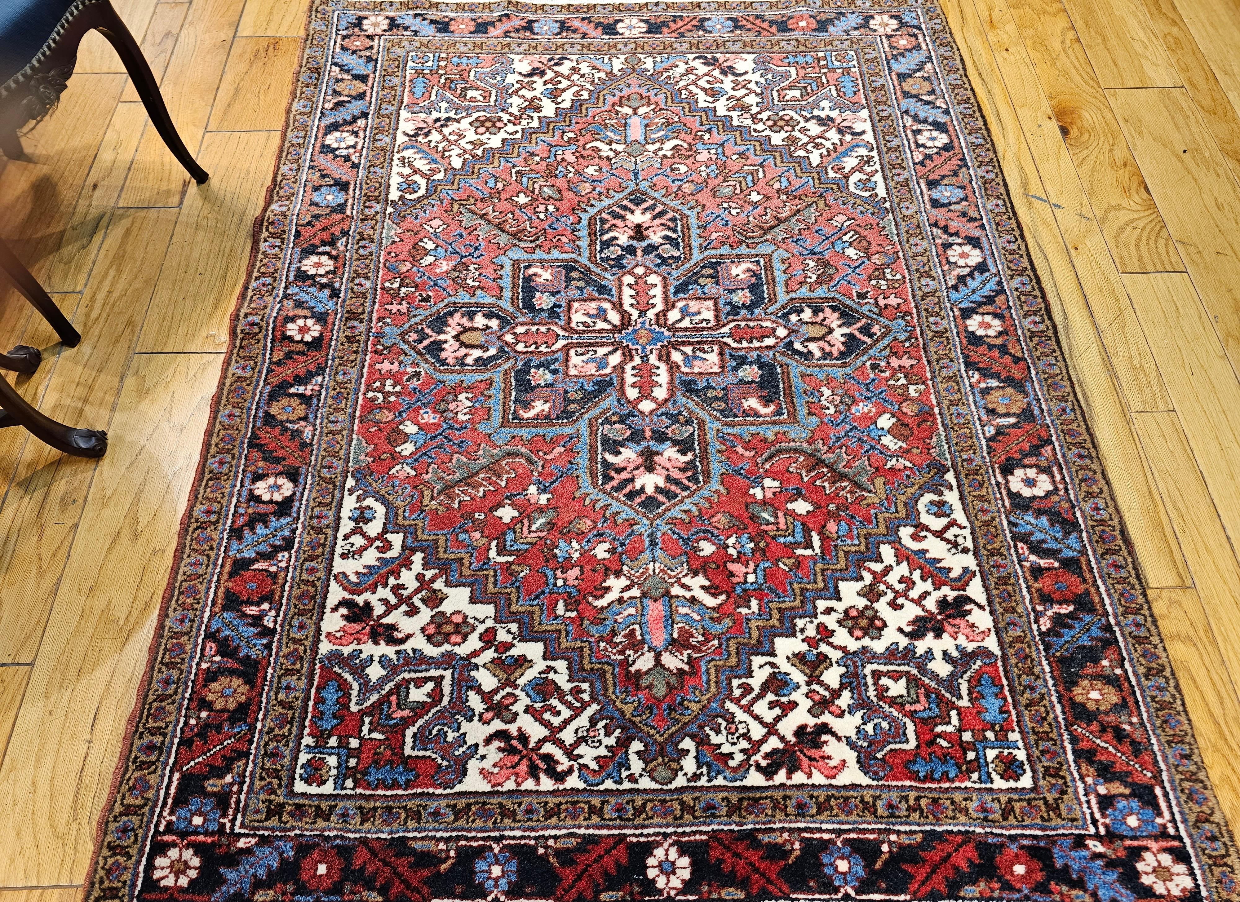  Vintage Persian Heriz area rug in a medallion pattern from the 2nd quarter of the 1900s. Beautiful geometric design set in a red and cream color field with a central medallion in navy blue.  The primary border is in navy blue with leaf designs in 