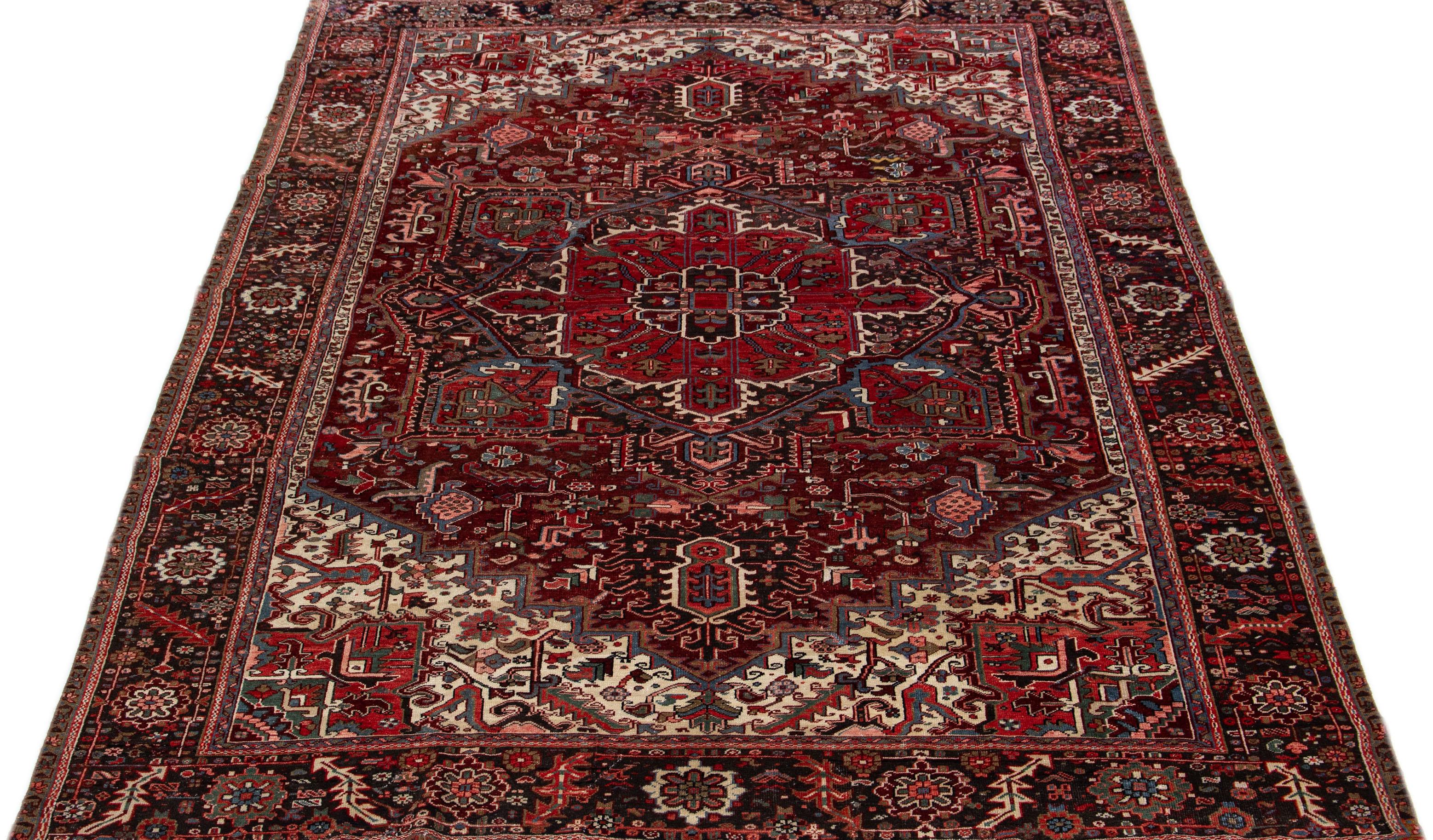 This is a stunning vintage Persian Heriz rug, artfully handcrafted using wool and featuring a vibrant red color field. The rug boasts an attractive brown frame with bright accents, cleverly arranged in an all-over geometric medallion pattern that