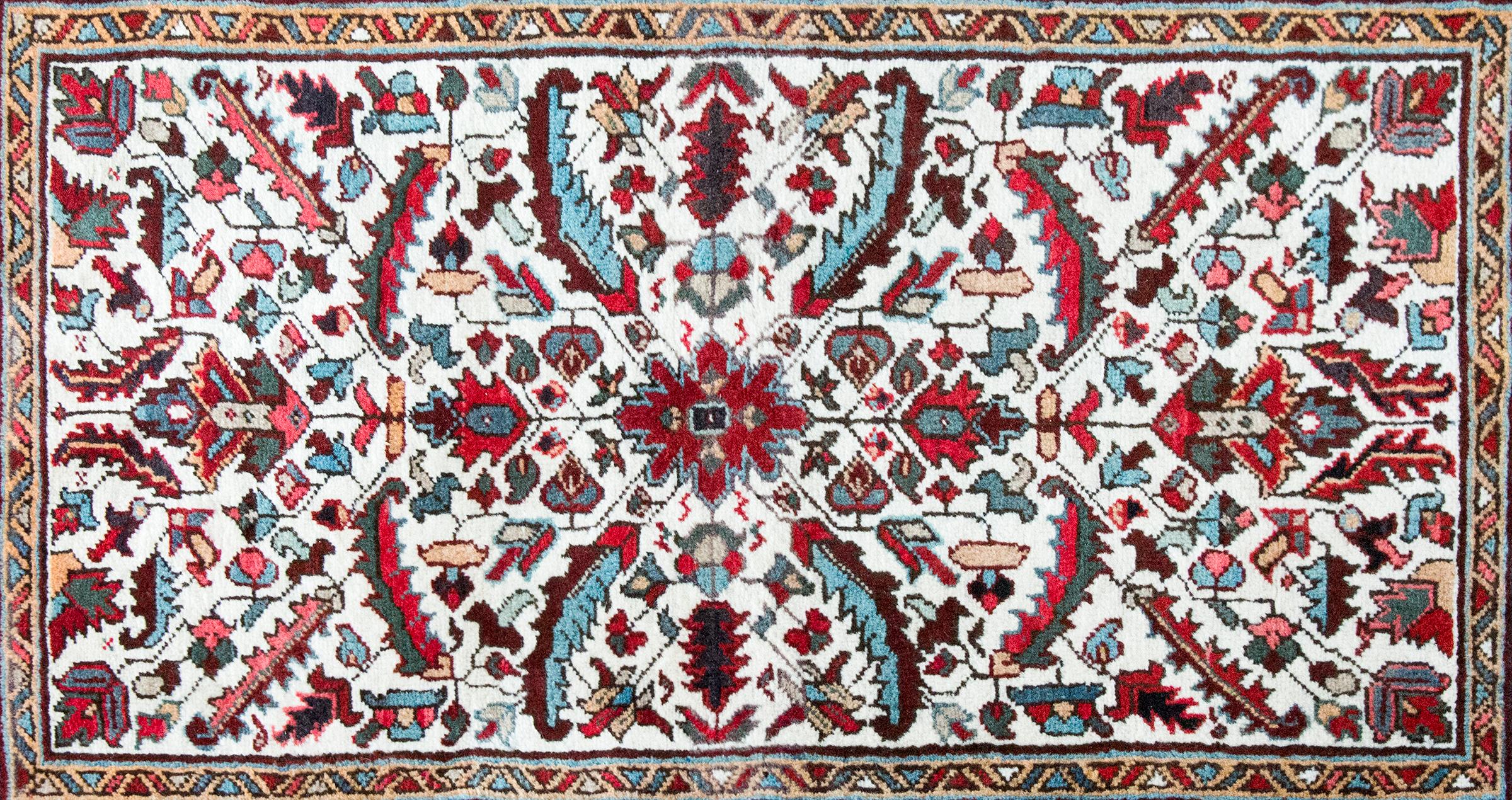 A wonderful vintage Persian Heriz rug with a simple mirrored pattern with a central floral medallion flanked by bathing leaves, scrolling vines, and more stylized flowers, surrounded by a border with a central floral stripe flanked by pairs of