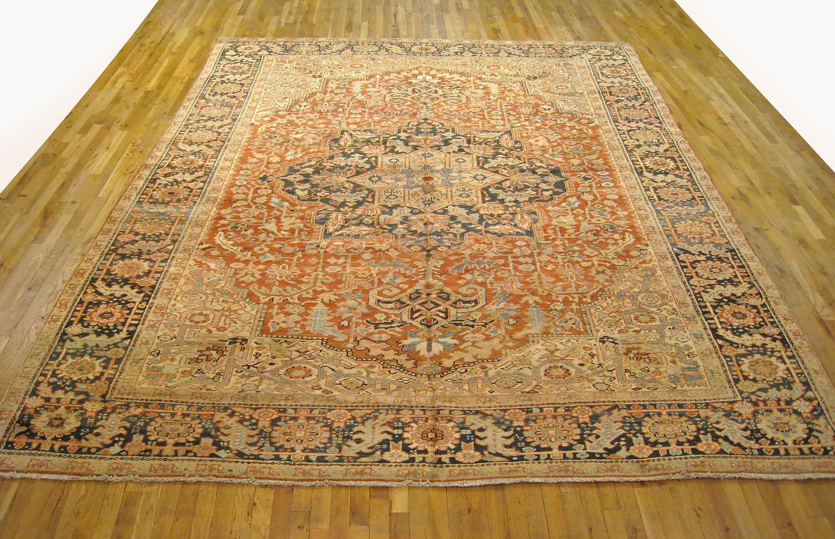 A vintage Persian Heriz oriental carpet, size 12'6 x 9'7, circa 1930. This handsome hand-woven geometric rug features a soft red primary field, with a blue central medallion and softly hued corner spandrels. The central field is enclosed within a