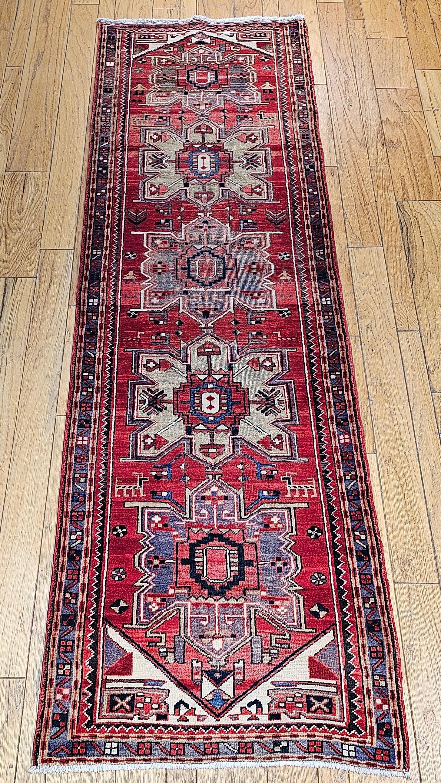 Ce magnifique chemin de table persan Heriz vintage, tissé dans le deuxième quart des années 1900, présente un médaillon géométrique classique sur un fond rouge antique. Le chemin de table présente cinq médaillons audacieux en forme de diamant,