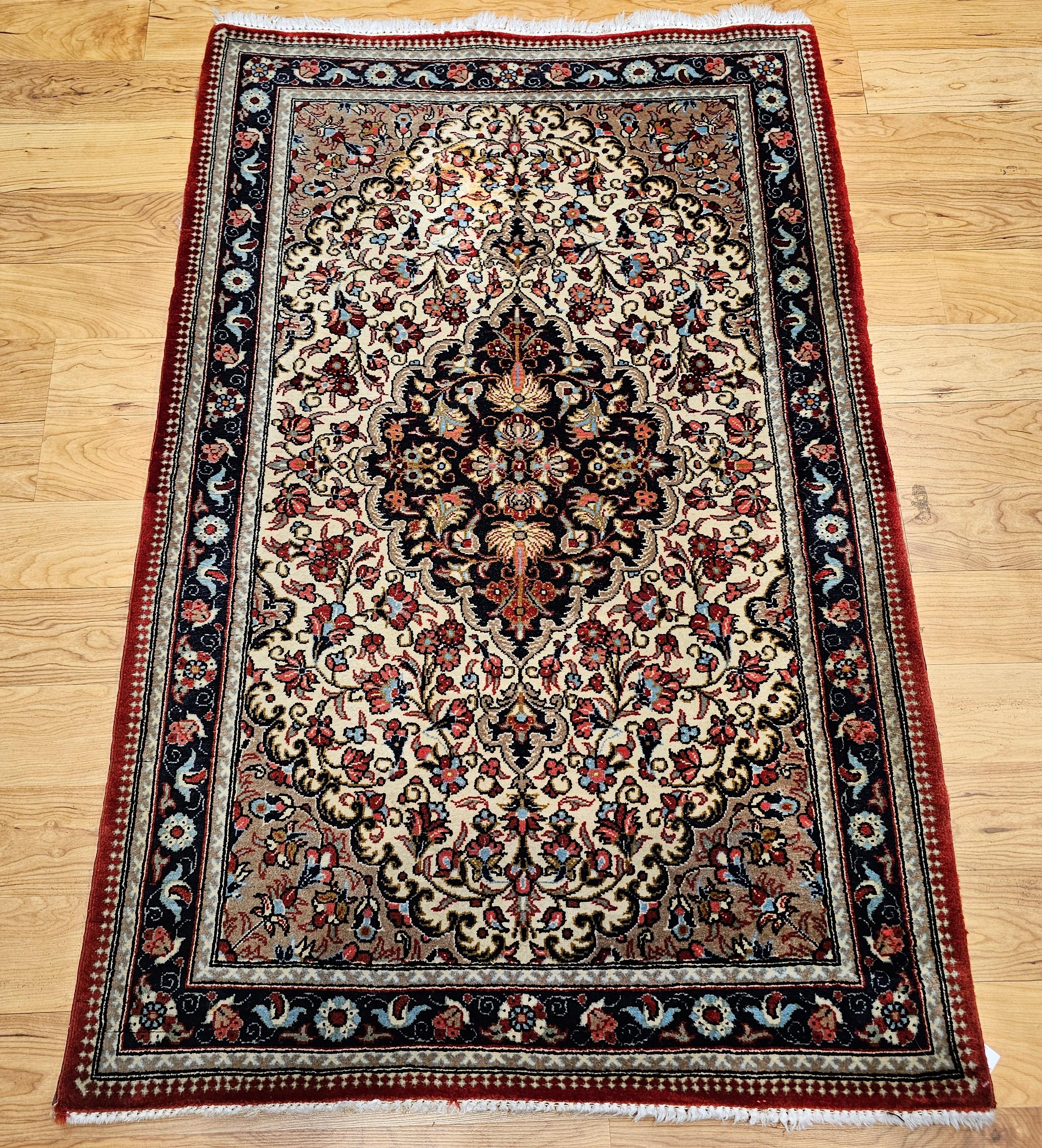 Vintage hand knotted Persian Isfahan area rug from the 3rd quarter of the 1900s.  The beautiful hand-knotted  rug has a floral pattern set on an ivory color field with a central medallion in navy blue with design accent colors in red, blue, green,