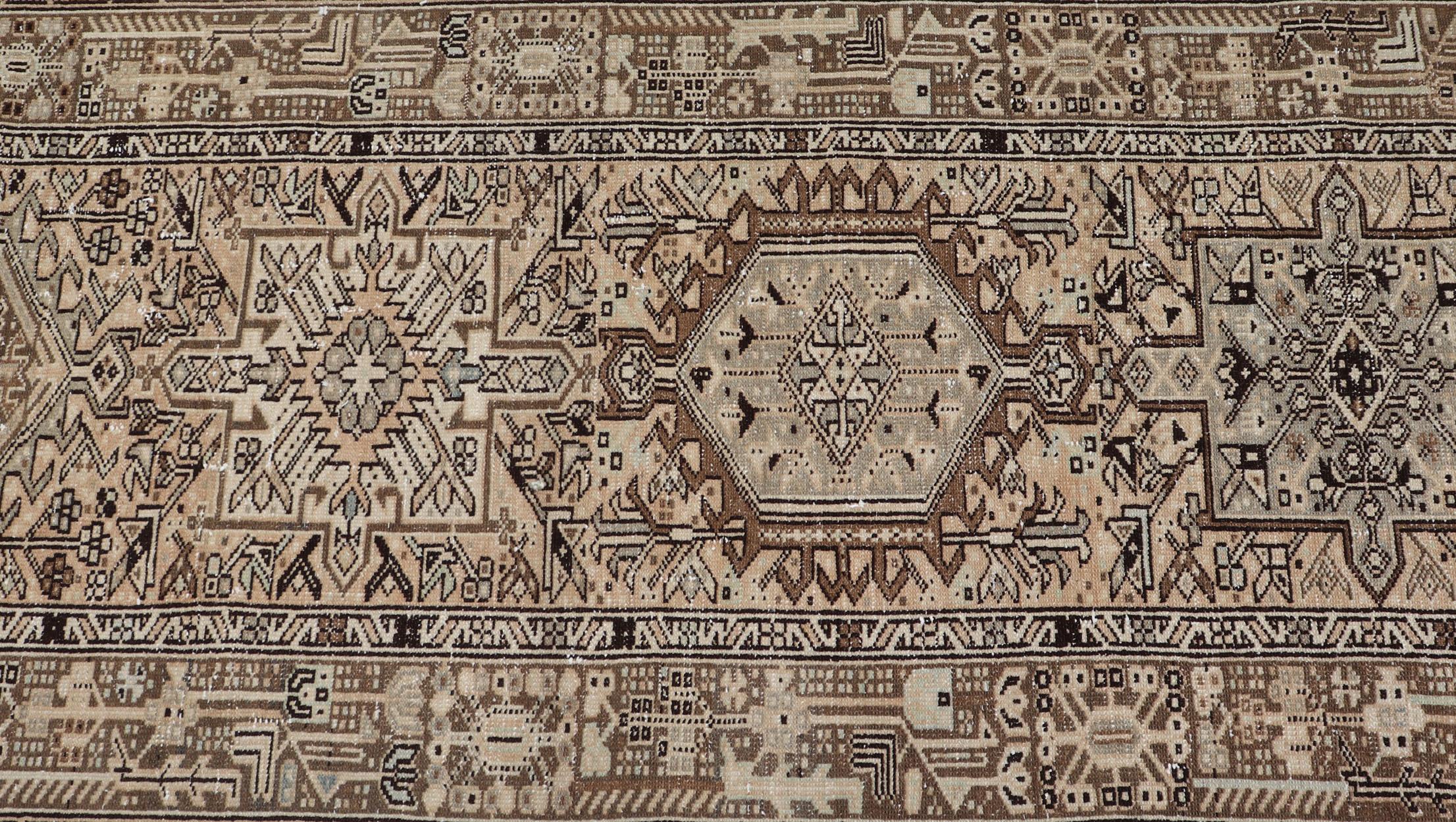 This vintage 1940's Karadjeh features brown and sandy tones and majestic medallions within the field. The wide banded border holds a motif design that repeats around the entirety of the piece. This treasure holds many details and would be a