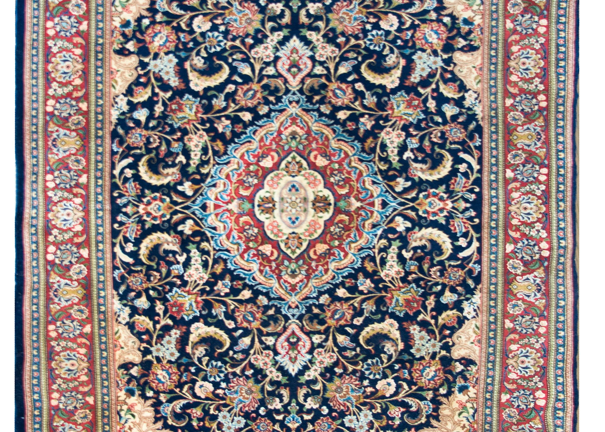 A beautiful mid-20th century Persian Kashan rug with a traditional central floral medallion living amidst a field of large-scale flowers and scrolling vines, and surrounded buy a wide repeated floral patterned central stripe flanked by pairs of