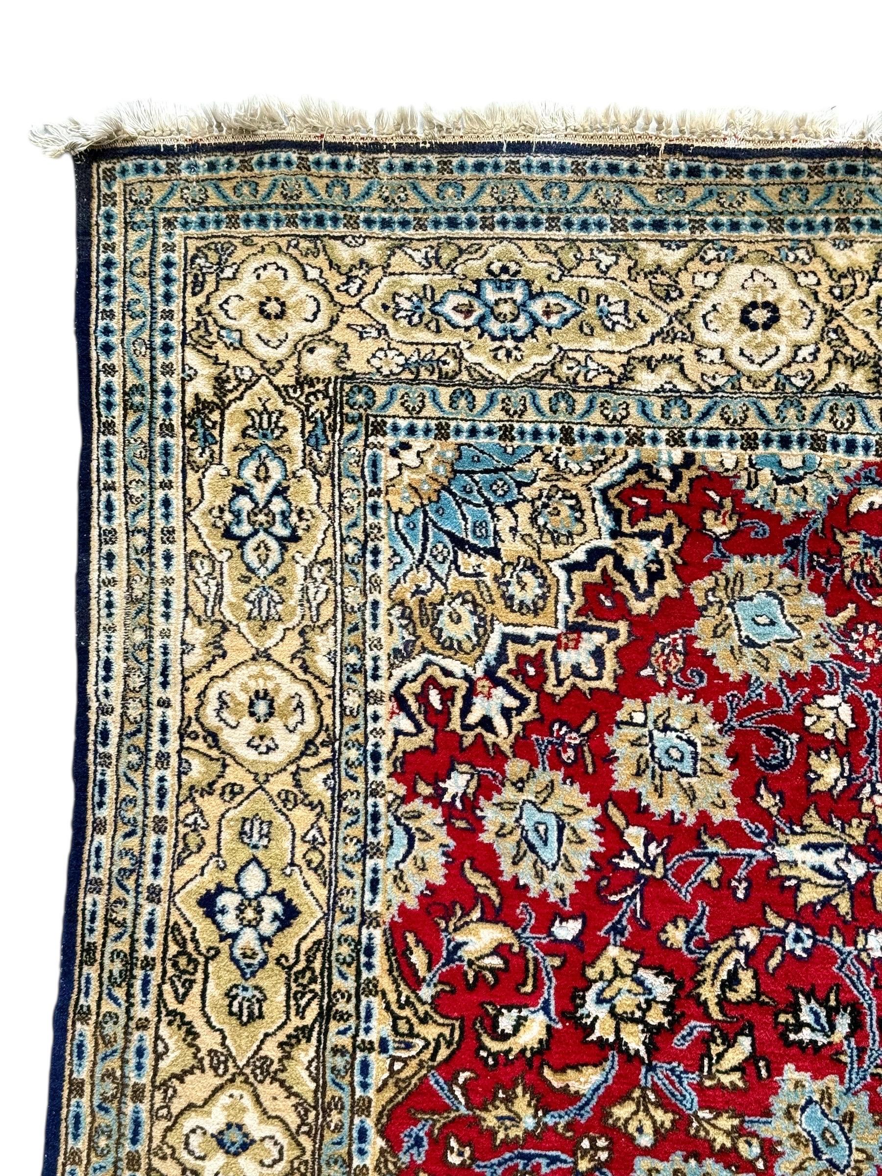 This exquisite vintage Persian Kashan rug features a classic floral medallion design set against a rich crimson red field, framed by an elegant border in shades of ivory, blue, and gold. Entirely hand-knotted in fine wool, this piece showcases the