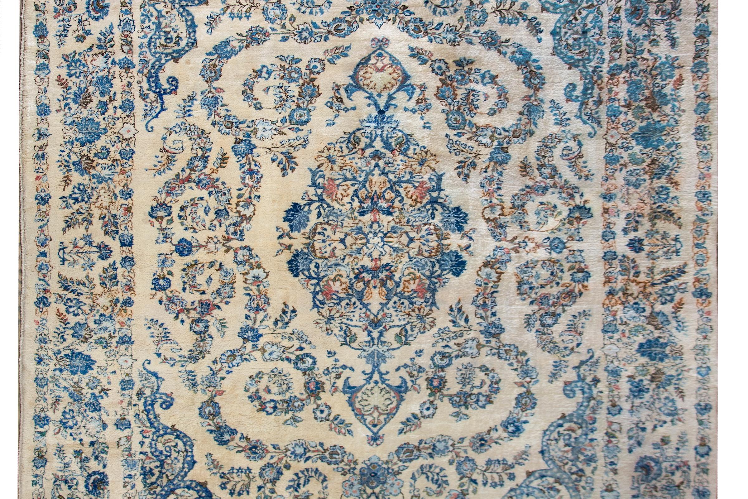 A beautiful mid-20th century Persian Kashmir rug with a large central floral medallion amidst a field of more flowers and surrounded by a border of even more flowers, all woven in light and dark indigo, pink, green, and white set against an ivory