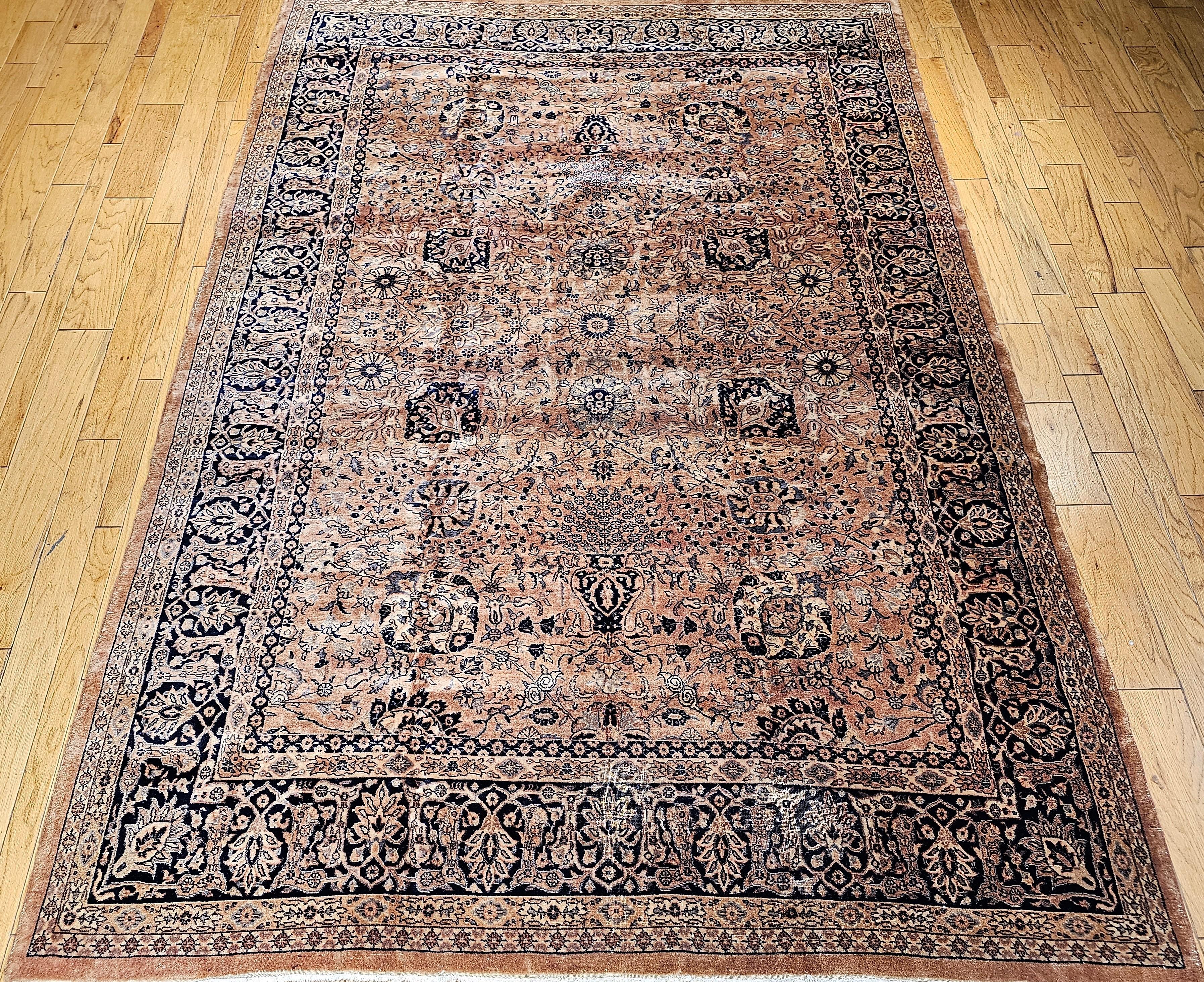 Vintage room-size Kerman Vase carpet from the mid-1900s.  The rug has a camelhair or apricot color background with an all-over trellis of leafy vines, palmettes, and vases issuing floral sprays within a black color flowerhead and palmette border.