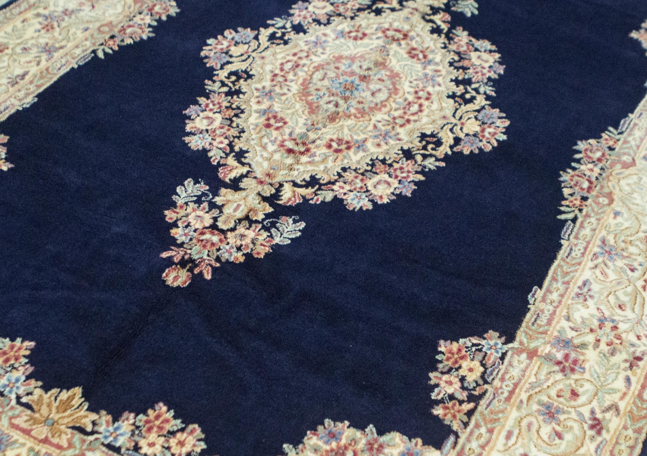 Tappeto persiano vintage Kerman del 1940 circa. Su un meraviglioso fondo blu intenso si trova un medaglione con disegni dettagliati di fiori estivi che si ripete nel bordo principale per dare a questo tappeto un senso di forza mescolato alla