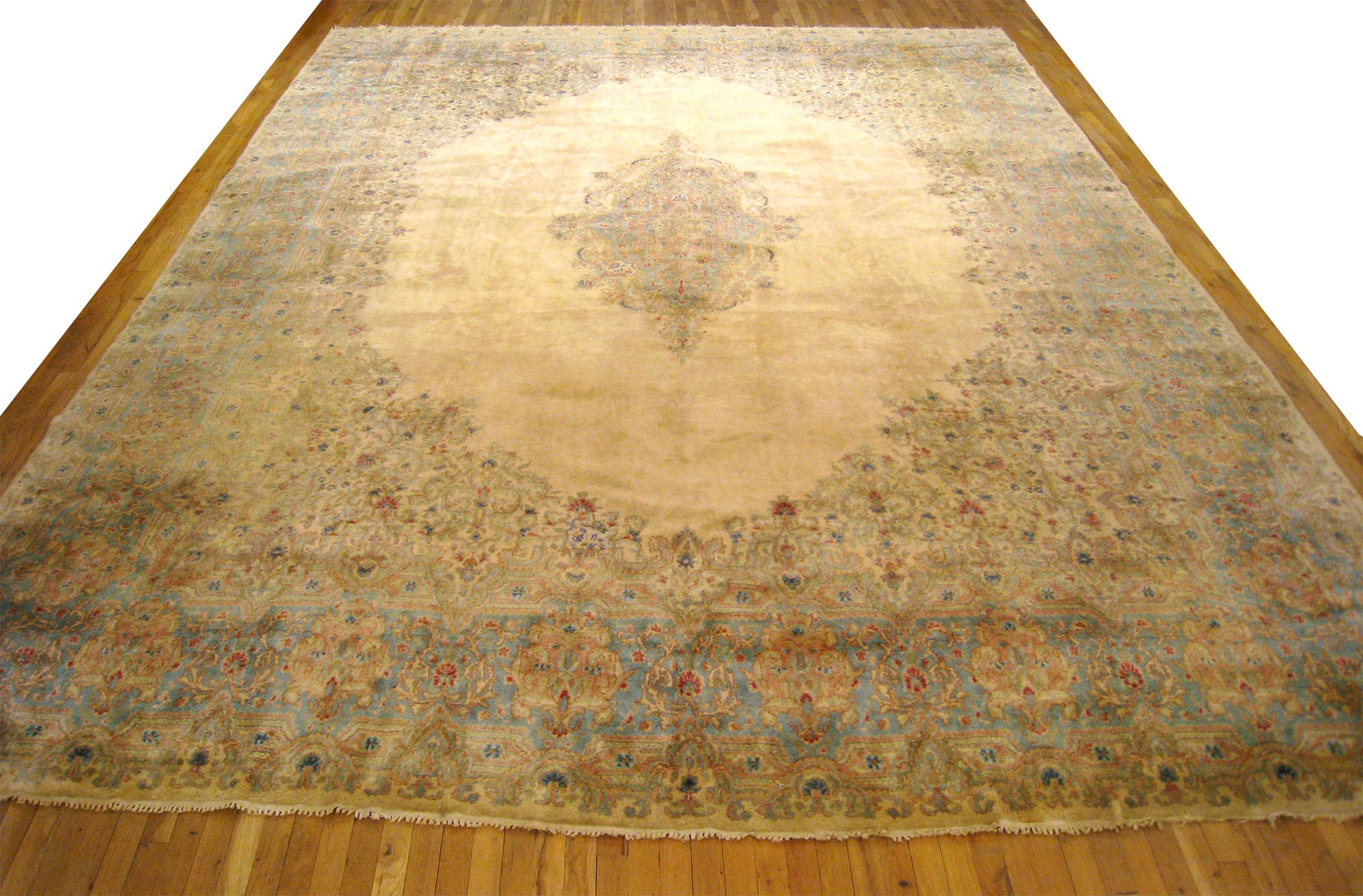 Vintage Persian Kerman rug, circa 1950, size 15'4 H x 11'6 W. This semi-antique hand knotted Persian rug features a striking open ivory central field, with a softly hued floral array in the corners and outer border. A small medallion punctuates the
