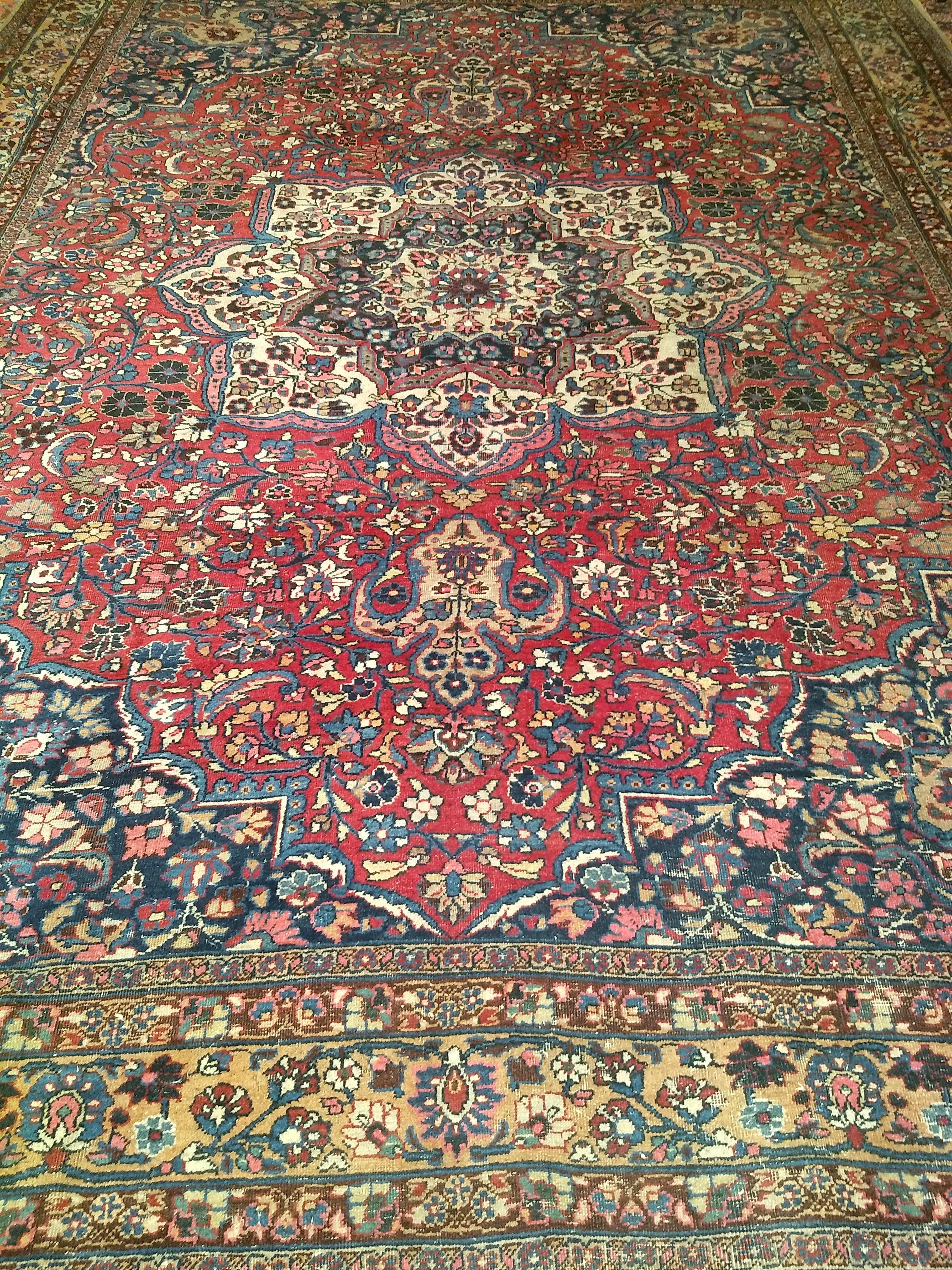 Room Size Persian Khorassan in a floral design with a central medallion from the early 1900s.  The design is set in a rich crimson red field color.  The main design consists of flowers and branches in various colors including red, green, pink,