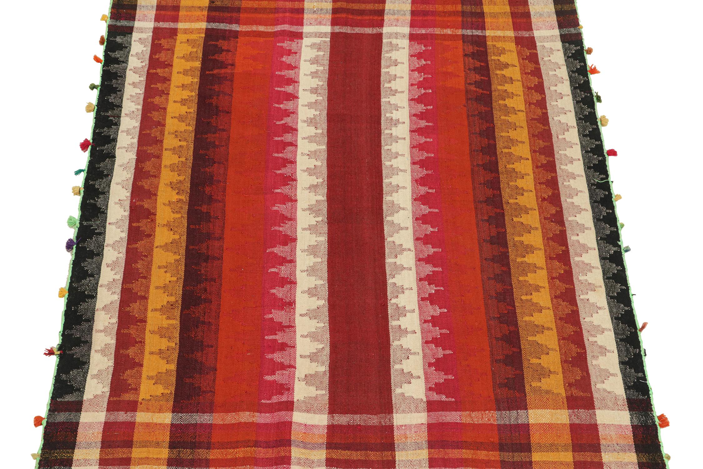 This vintage 5x7 Persian kilim is a mid-century tribal rug, handwoven in wool circa 1950-1960.

The design enjoys vertical stripes and plaid borders relishing bright and warm red, black, white, orange, and gold tones. Keen eyes will further note