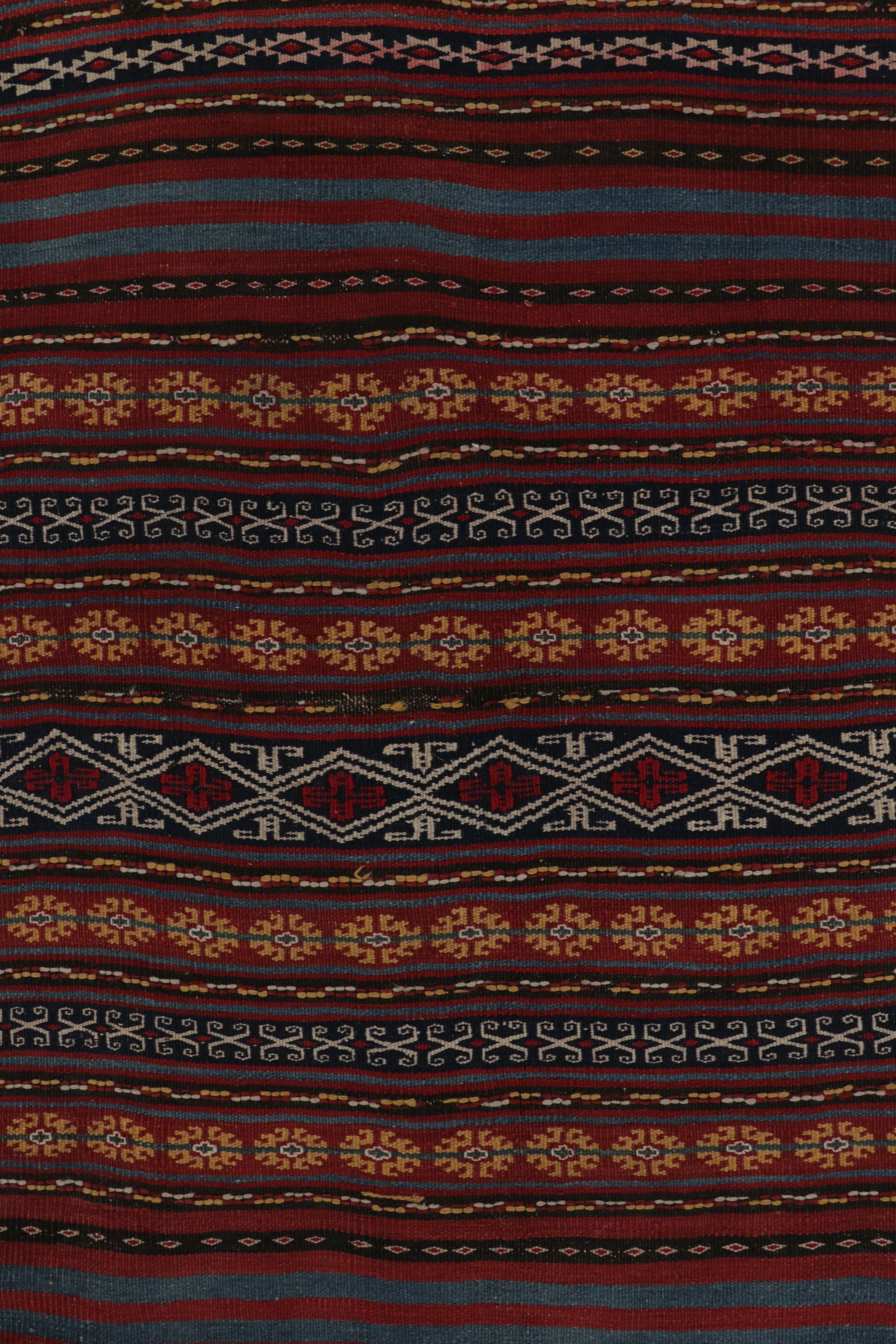 Realizzato con lana tessuta a mano intorno al 1950-1960, questo Kilim vintage 3x12 presenta una fitta fascia orizzontale e intricati motivi geometrici nei toni del rosso scuro, del prugna, del blu profondo e del beige. I designer e i collezionisti