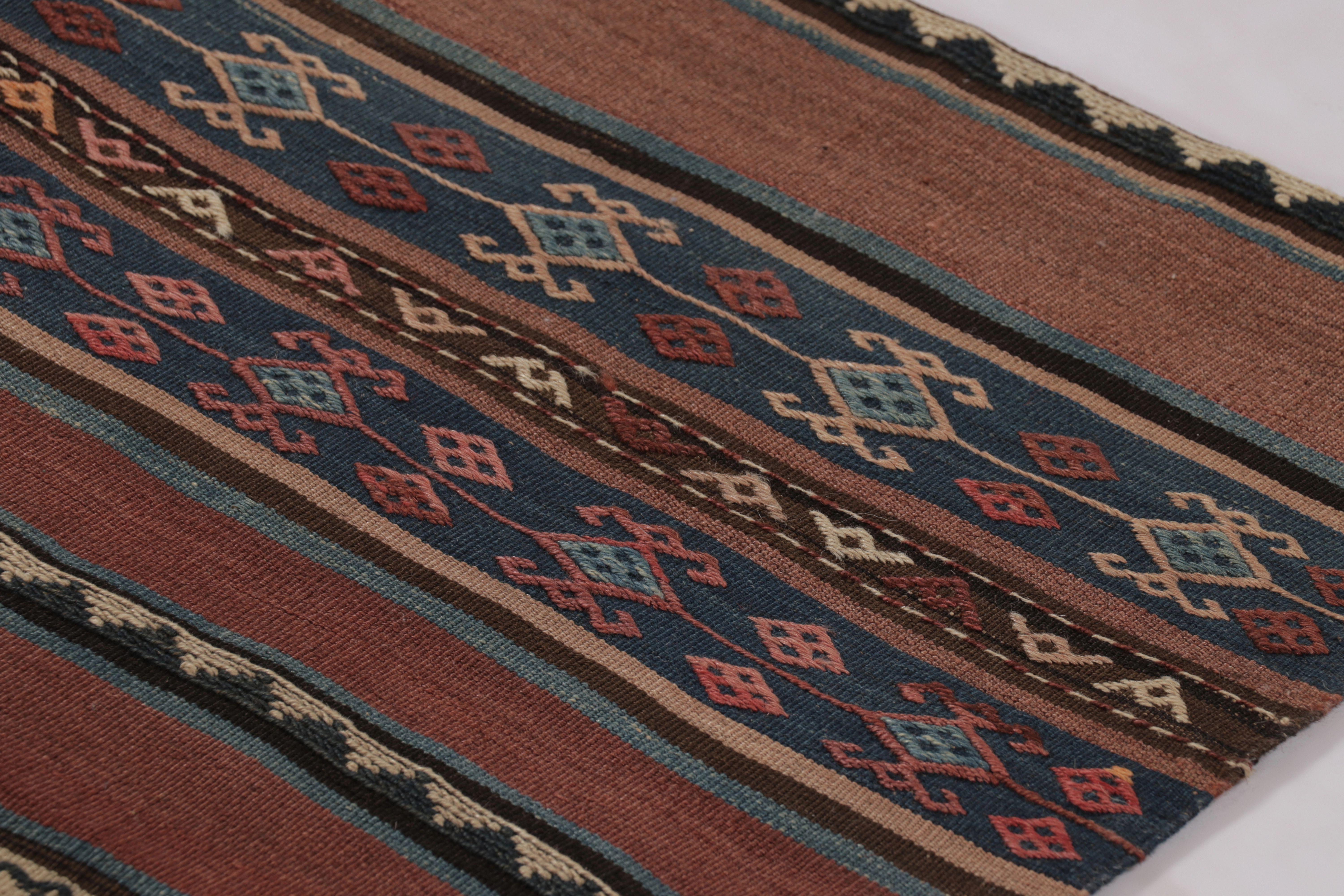 Made with handwoven wool circa 1950-1960, this 3x13 vintage Persian Kilim runner enjoys complex horizontal band and tribal geometric patterns in brick red, indigo, and brown tones. Designers and collectors alike will note this runner is one of a