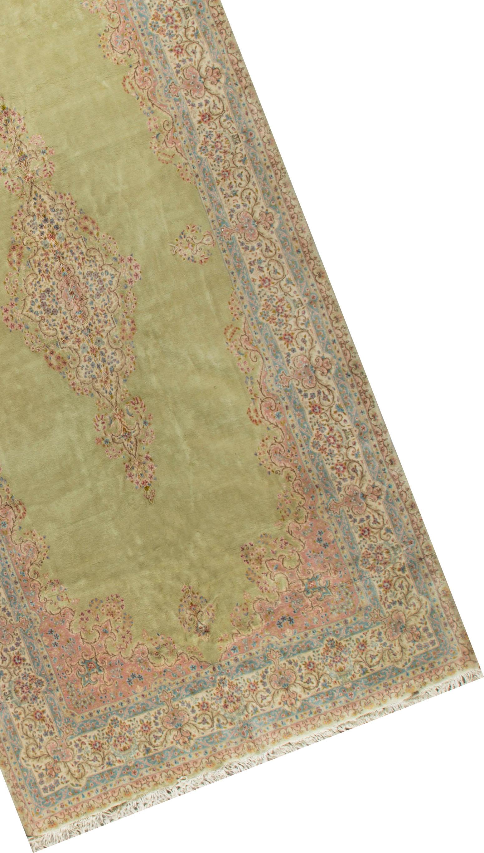 Persischer Kirman-Teppich im Vintage-Stil. Dieser außergewöhnliche Teppich mit seiner ungewöhnlichen Länge und Breite schafft einen dramatischen Auftritt in jedem Raum. Das zartgrüne Feld umschließt ein zentrales Medaillon mit floralen Motiven, die