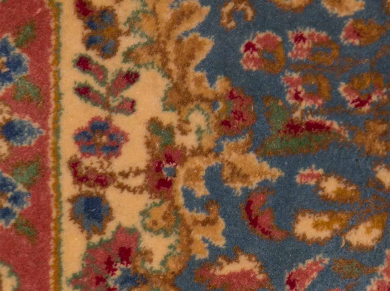 A delightful Kerman rug woven with exquisite detail, the red ground filled with weaving floral designs surrounding a central ivory and soft blue medallion bounded by a soft green main border and ivory and blue guard borders to give this rug a