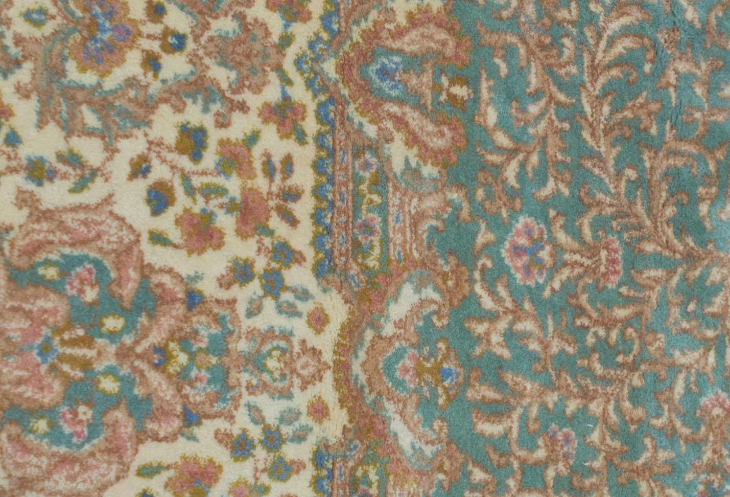 Un délicieux tapis de Kerman tissé avec des détails exquis, le fond rouge rempli de motifs floraux entourant un médaillon central ivoire et bleu doux délimité par une bordure principale vert doux et des bordures de garde ivoire et bleu pour donner à