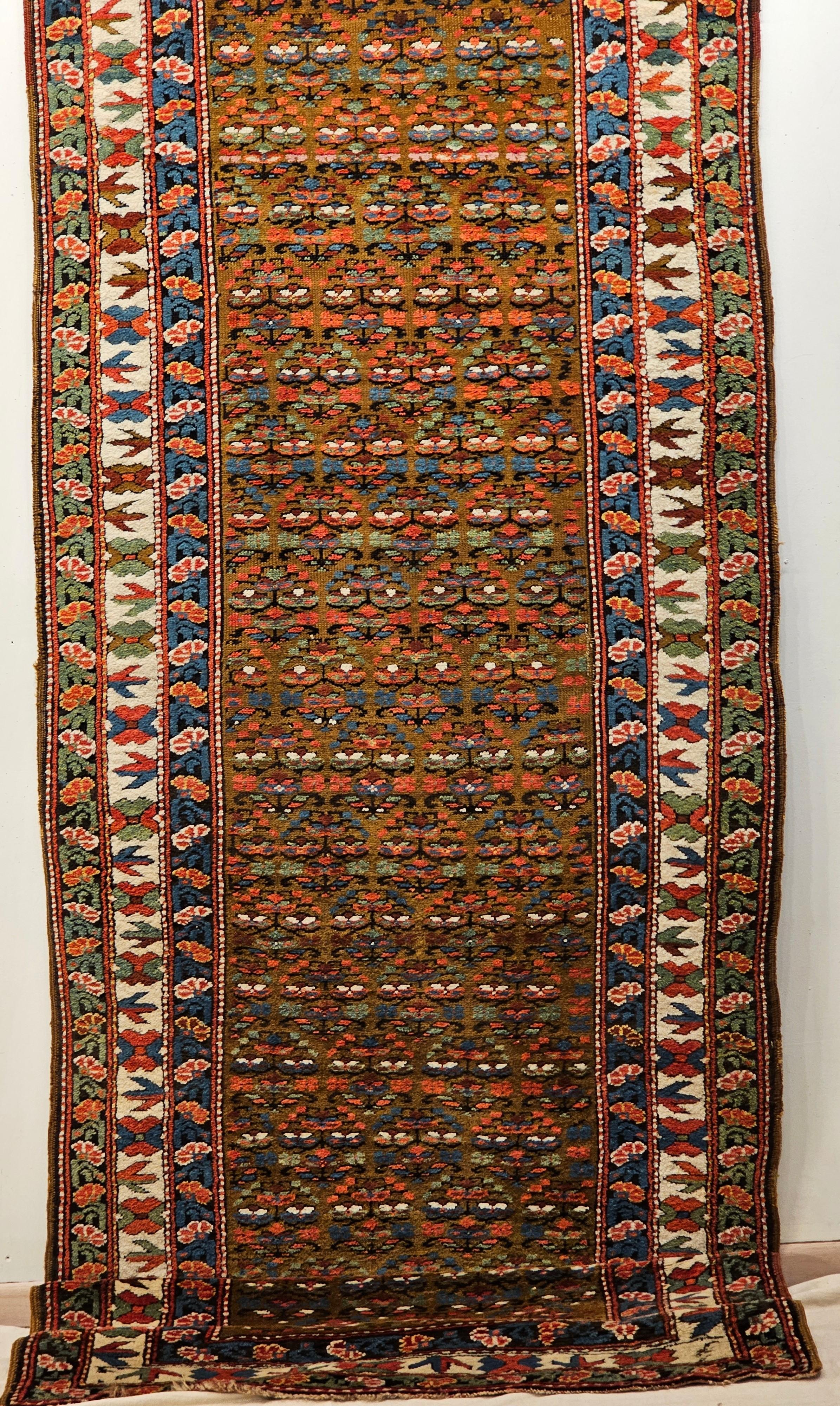 Persian Kurdish Camelhair runner in an allover small flower head pattern (a variation on paisley design) from the early 1900s. The field contains rows of the flower design in green, blue, red and ivory.  The rug has a wonderful triple border.  The