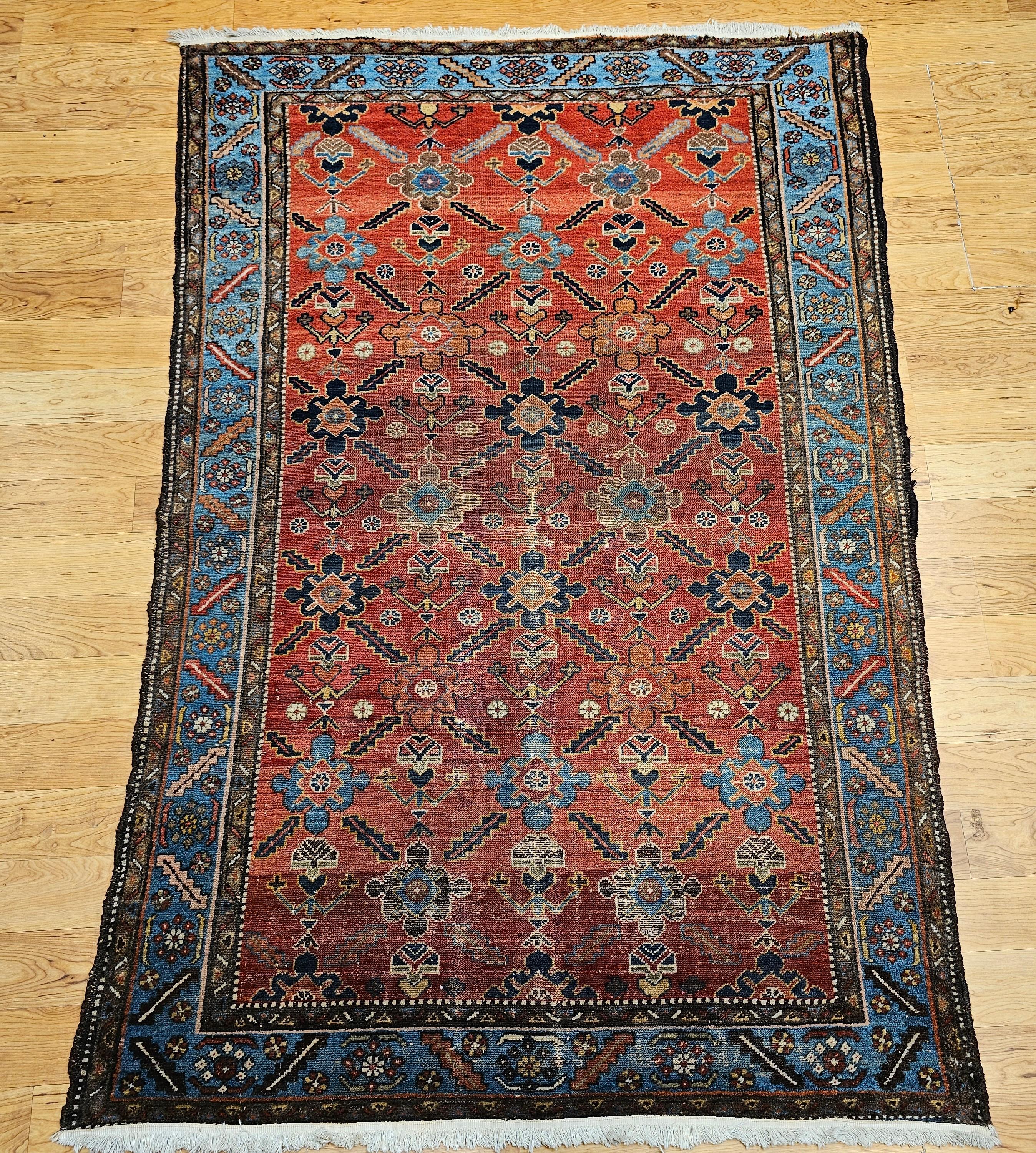 This exquisite vintage Persian Malayer rug, handwoven in the early 20th century, features a striking all-over geometric pattern rendered in a warm rust red field framed by a rich Persian blue border. The composition is elevated by nuanced accents of