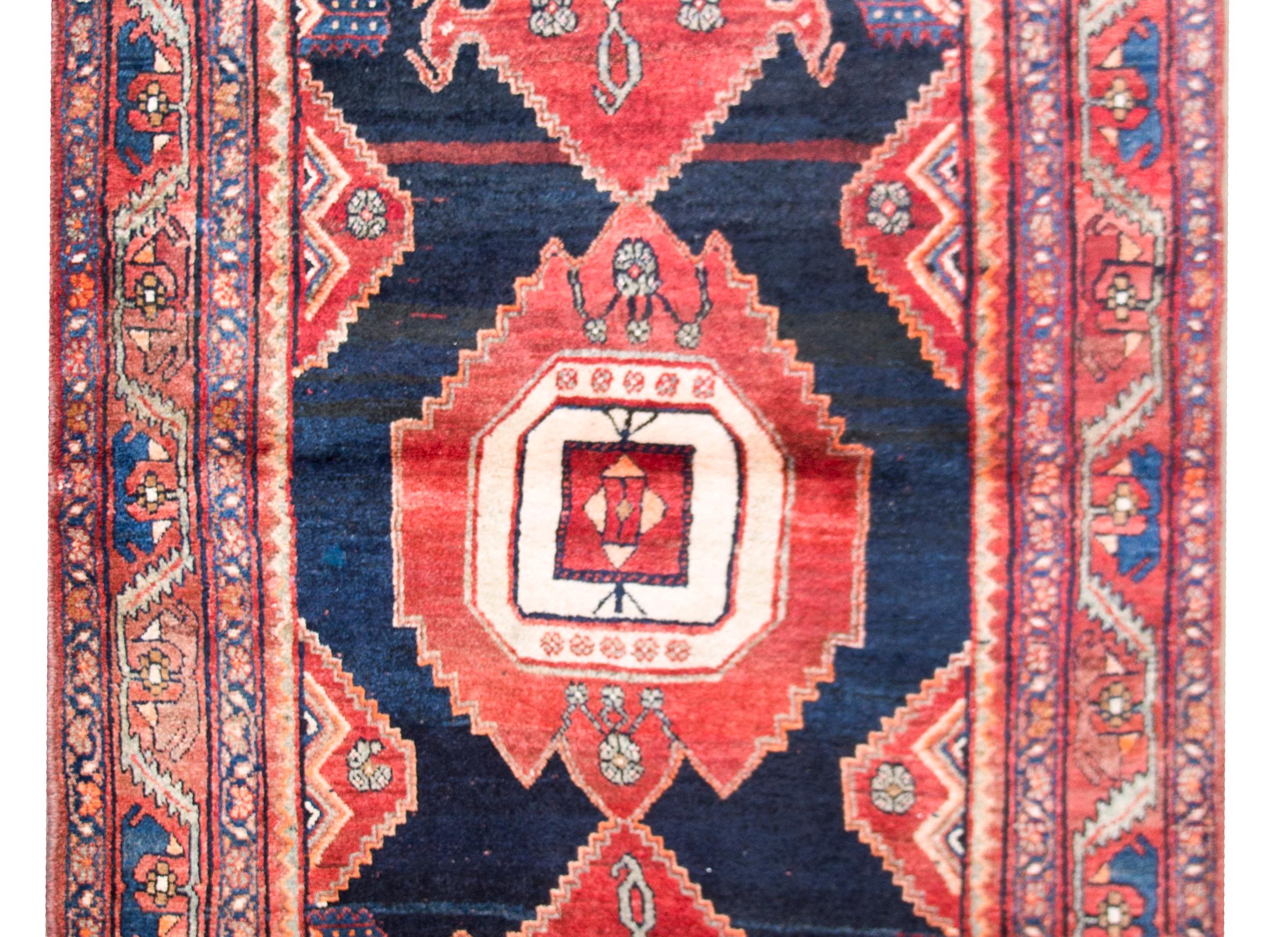 A wonderful early 20th century vintage Persian Mazleghan rug with bold geometric pattered medallions woven in crimson, white, orange, and gray, and set against an abrash indigo background, and surrounded by a border composed of multiple petite