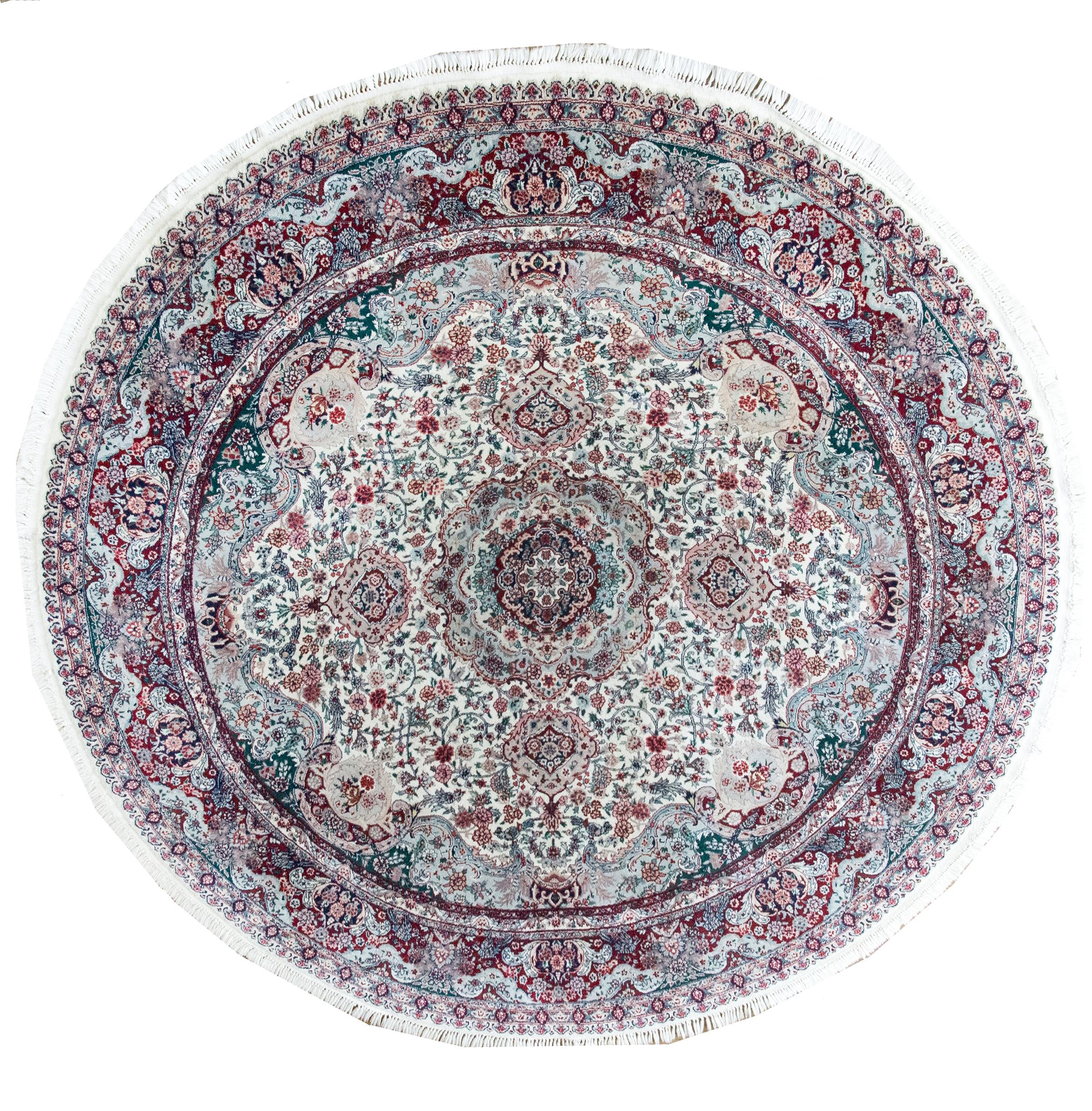 An unusual round late 20th century Persian Moud rug with an elaborately woven pattern with myriad flowers and scrolling vines radiating out from the central floral medallion, and all woven in varying shades of pinks, crimsons, greens, and creams.
