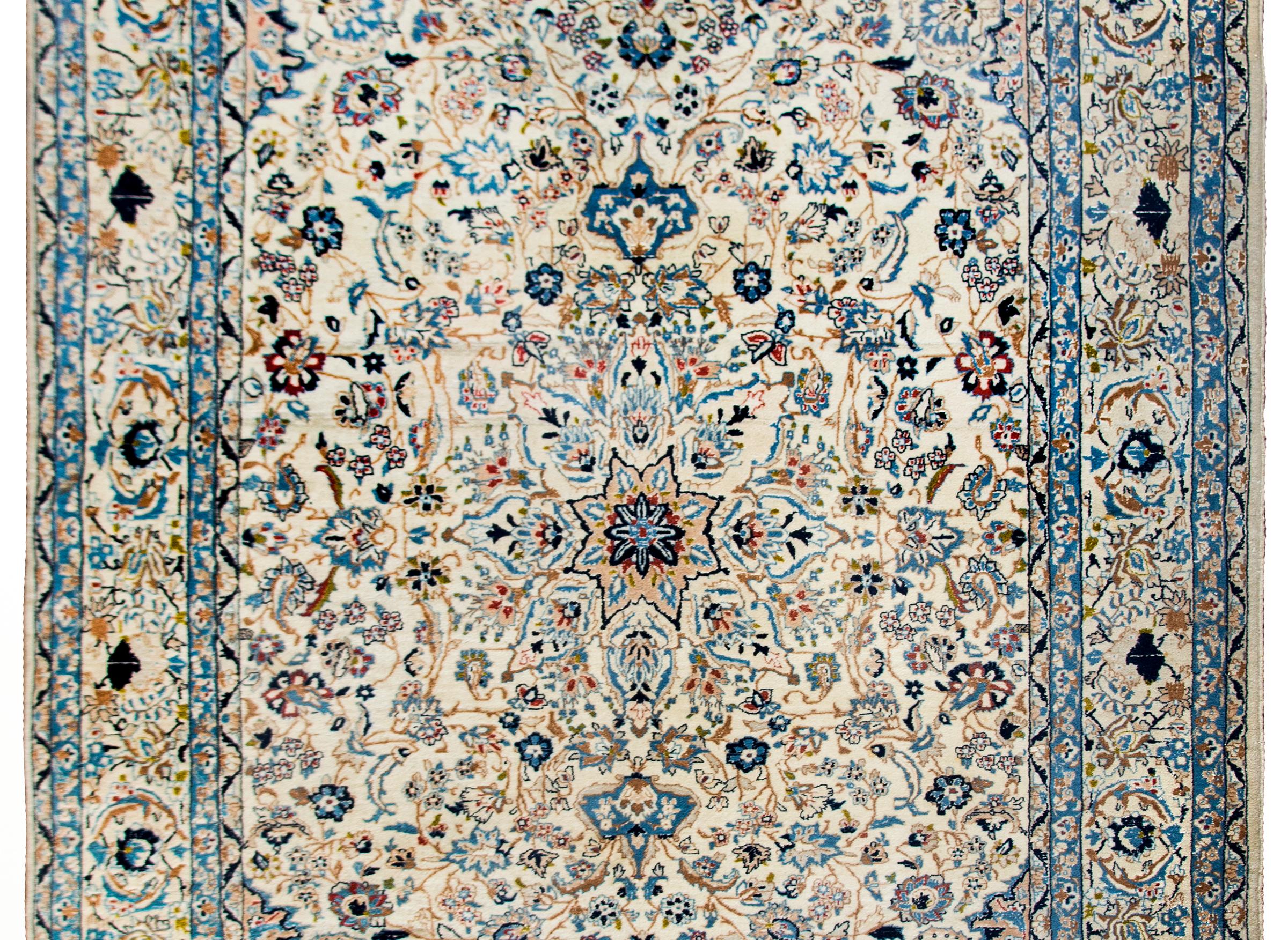 A wonderful late 20th century Persian Naein rug hand-woven in wool and silk with a beautiful densely woven scrolling vine and floral patterned field and surrounded by a complex border of more flowers and vines.