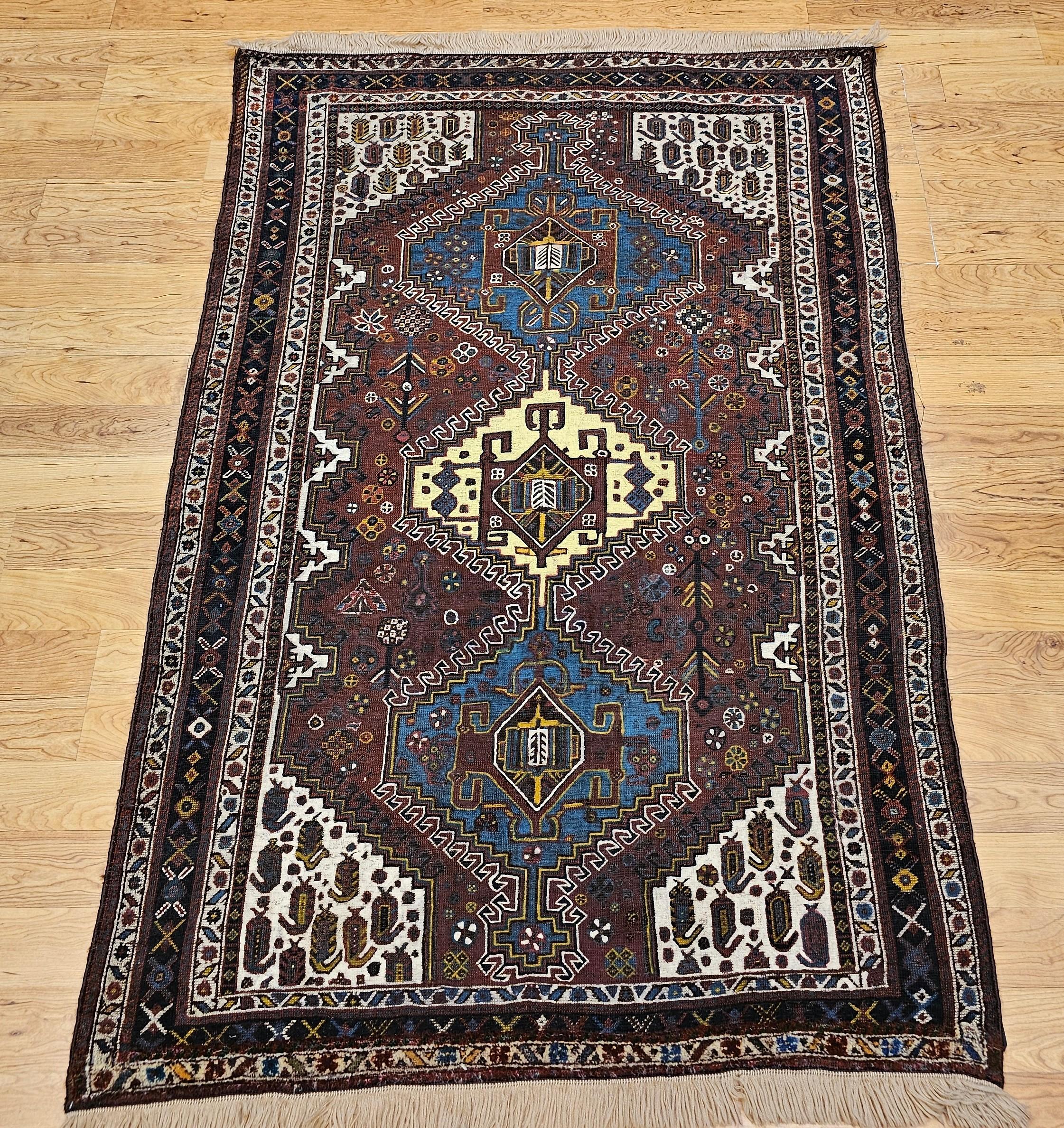 Magnifique tapis tribal persan Qashqai dans les tons rouge rouille, ivoire, bleu royal, jaune et marine, datant du début des années 1900.  Un triple médaillon bleu roi et jaune sur fond rouge foncé ou bordeaux couvre la majeure partie du centre du