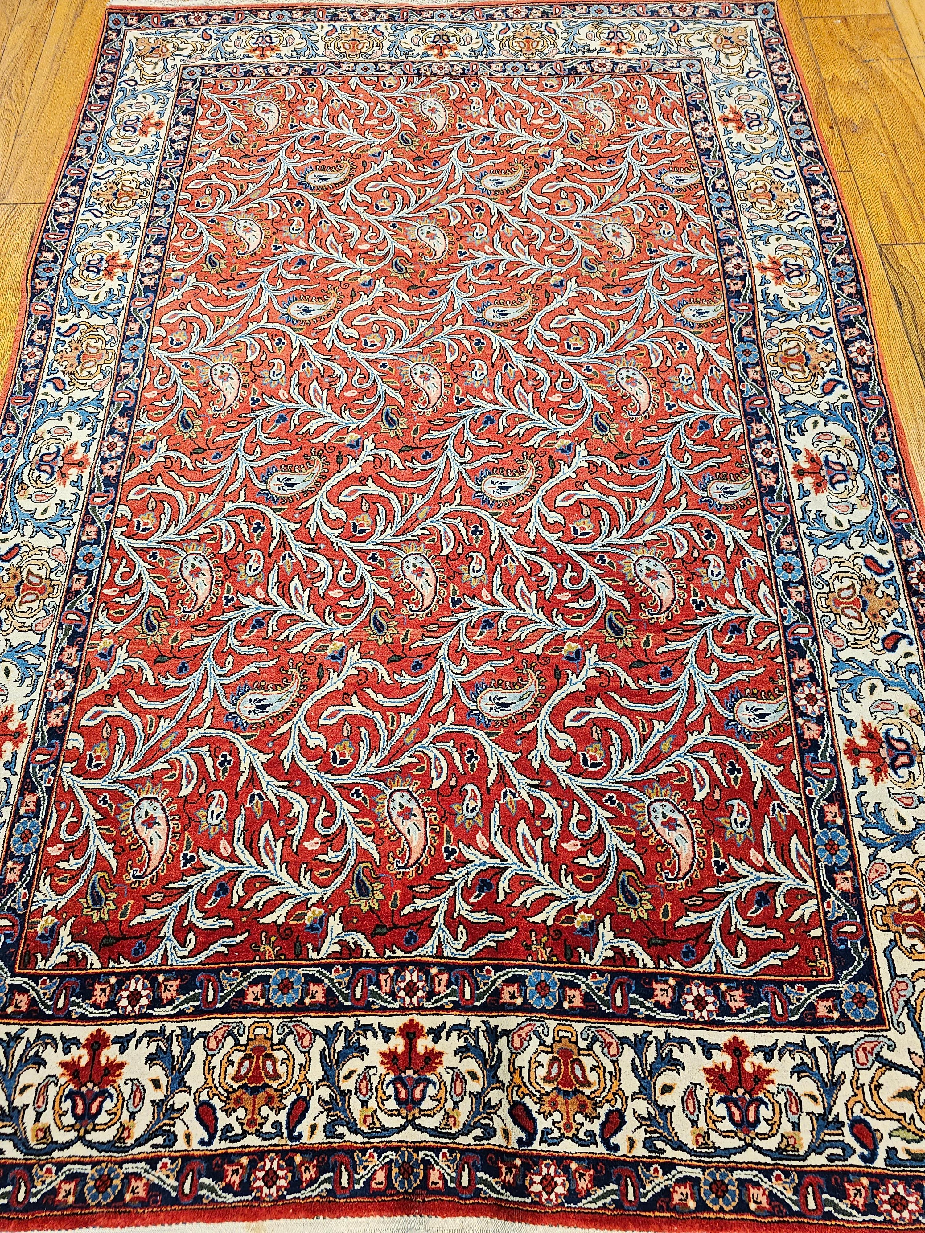 Un Qum persan vintage à motif de paisleys et de vignes sinueuses sur un riche fond rouge, datant du deuxième quart des années 1900.  Le tapis présente un motif all-over de vignes ondulantes et de formes cachemire dans un riche champ de couleur